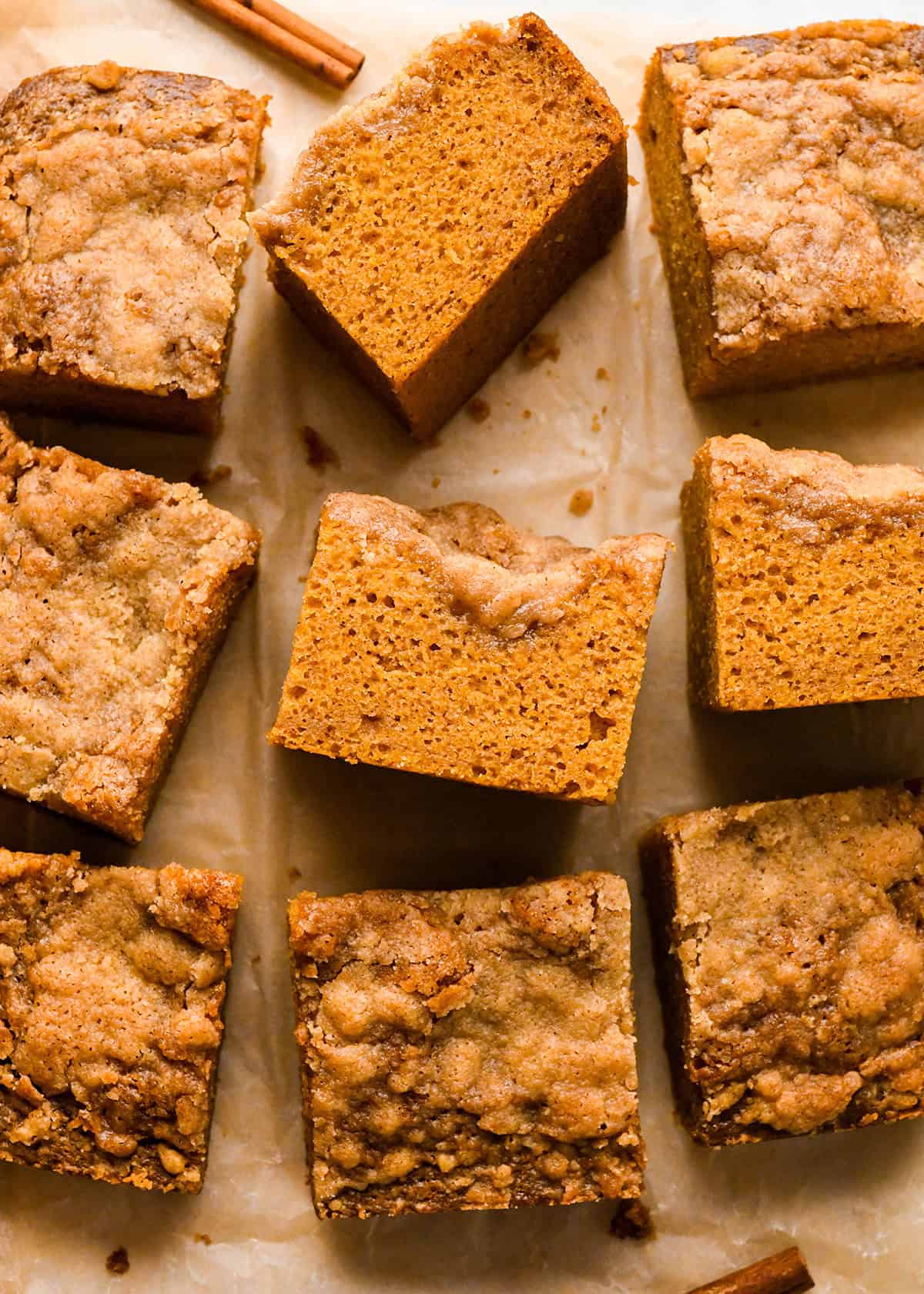 9 pieces of Pumpkin Coffee Cake, 3 on their side so the texture is visible on parchment paper with a cinnamon stick