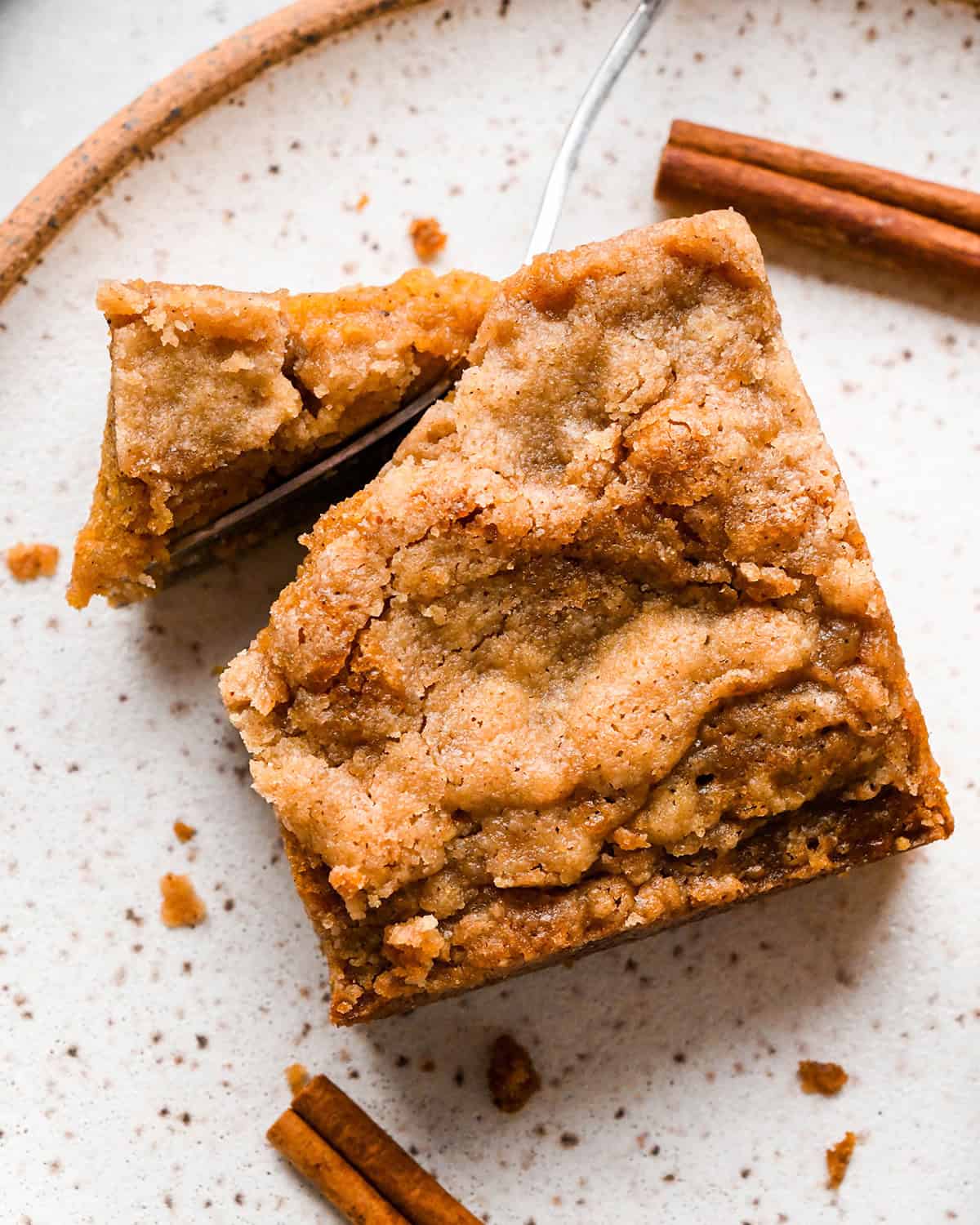 close up of a fork taking a bite of Pumpkin Coffee Cake on a plate with a cinnamon stick nearby