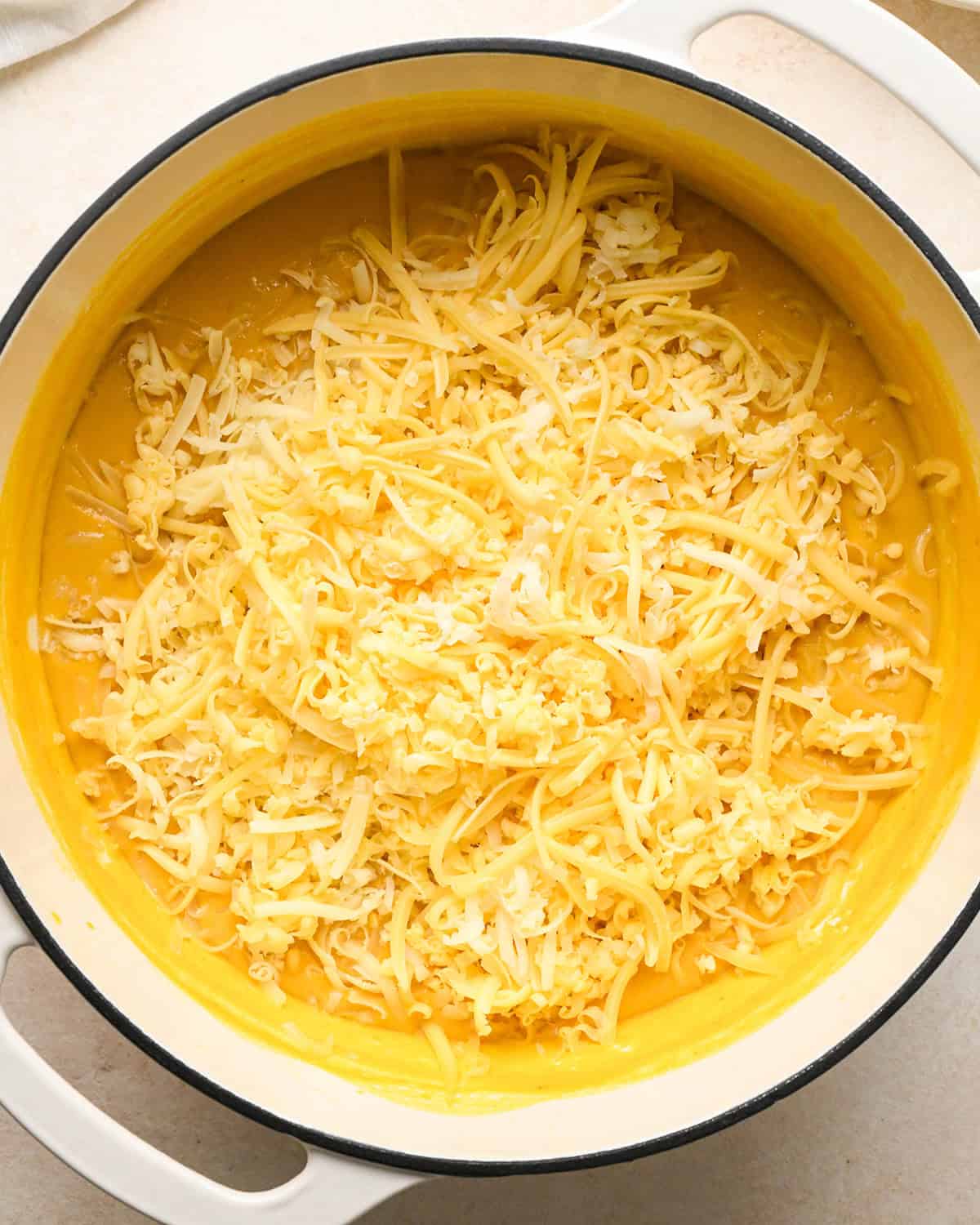 cheese added to the pumpkin mac and cheese sauce in a white pot before stirring