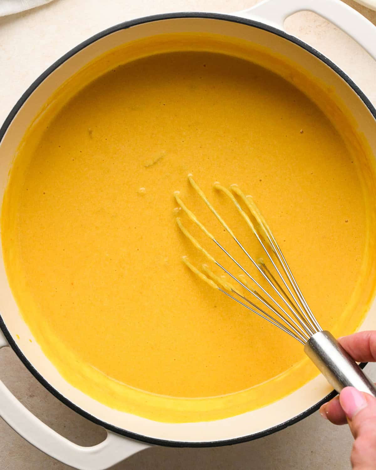 cheesy pumpkin macaroni and cheese sauce being whisked in a white pot with a silver whisk