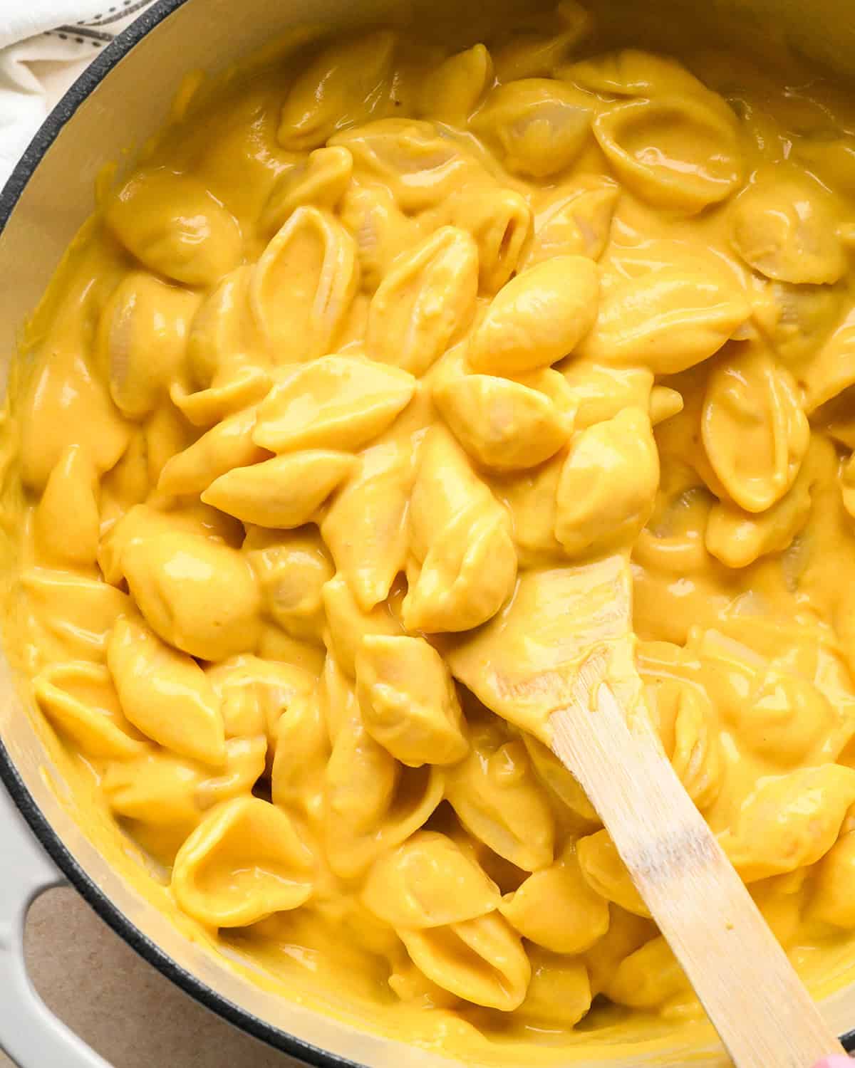 final pumpkin macaroni and cheese stirred with a wooden spoon in a white pot 