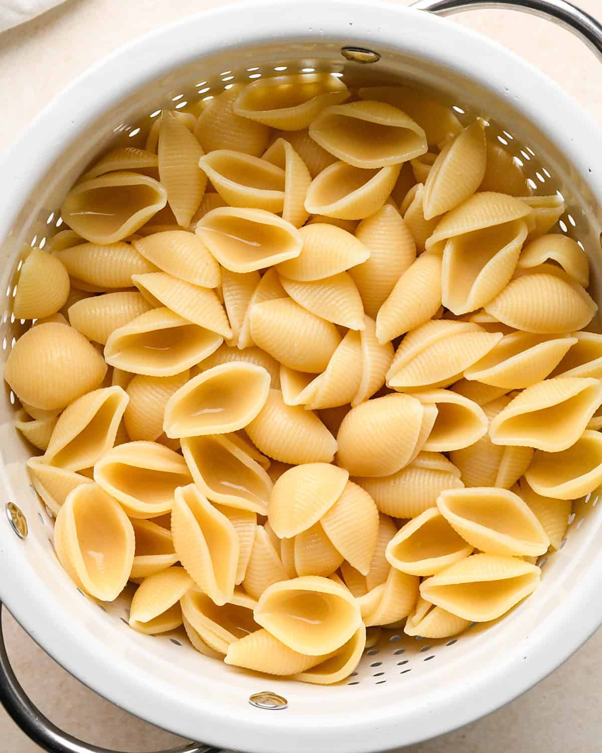 cooked shell pasta in a white colander with metal handle to be used to make pumpkin mac and cheese