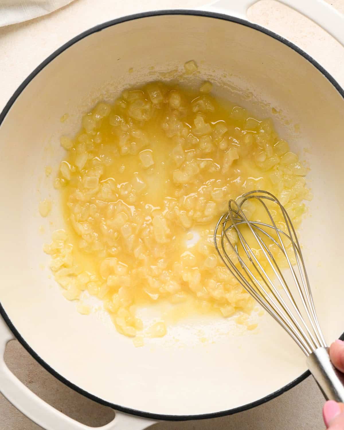 a whisk whisking flour and salt in to the melted butter and onion mixture in a white pot to make pumpkin macaroni and cheese
