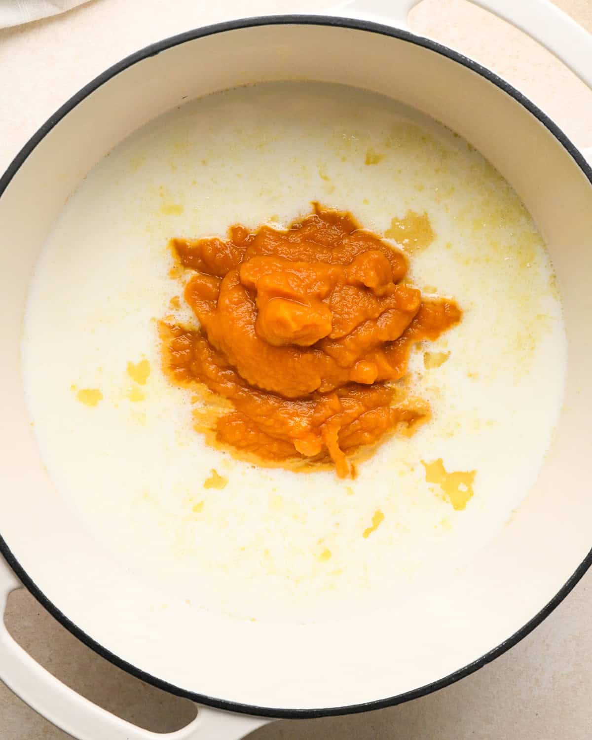 pumpkin and whole milk added to the flour butter onion mixture in a white pot before stirring
