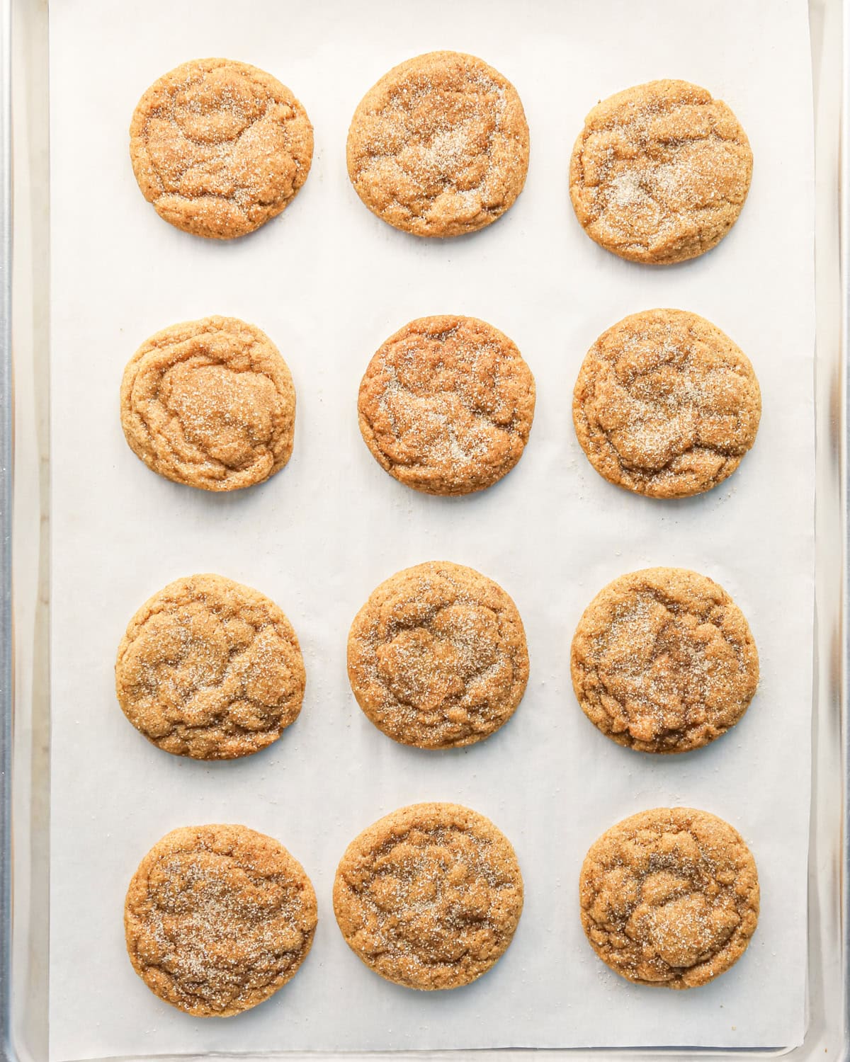 12 baked pumpkin snickerdoodle cookie dough balls covered in cinnamon sugar on a silver baking sheet lined with parchment paper 
