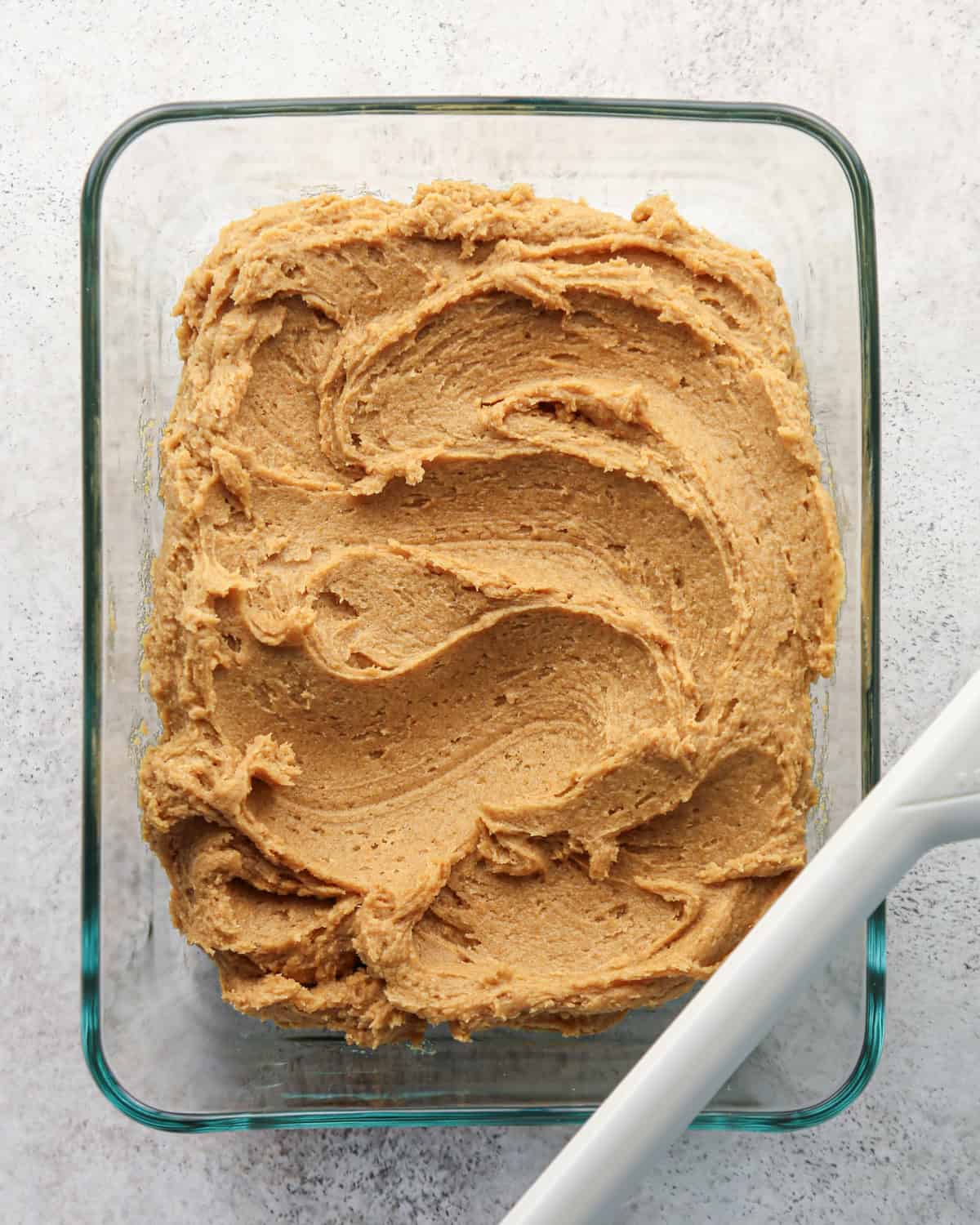 pumpkin snickerdoodle cookie dough in a rectangular glass container on a gray surface with a white spatula before chilling