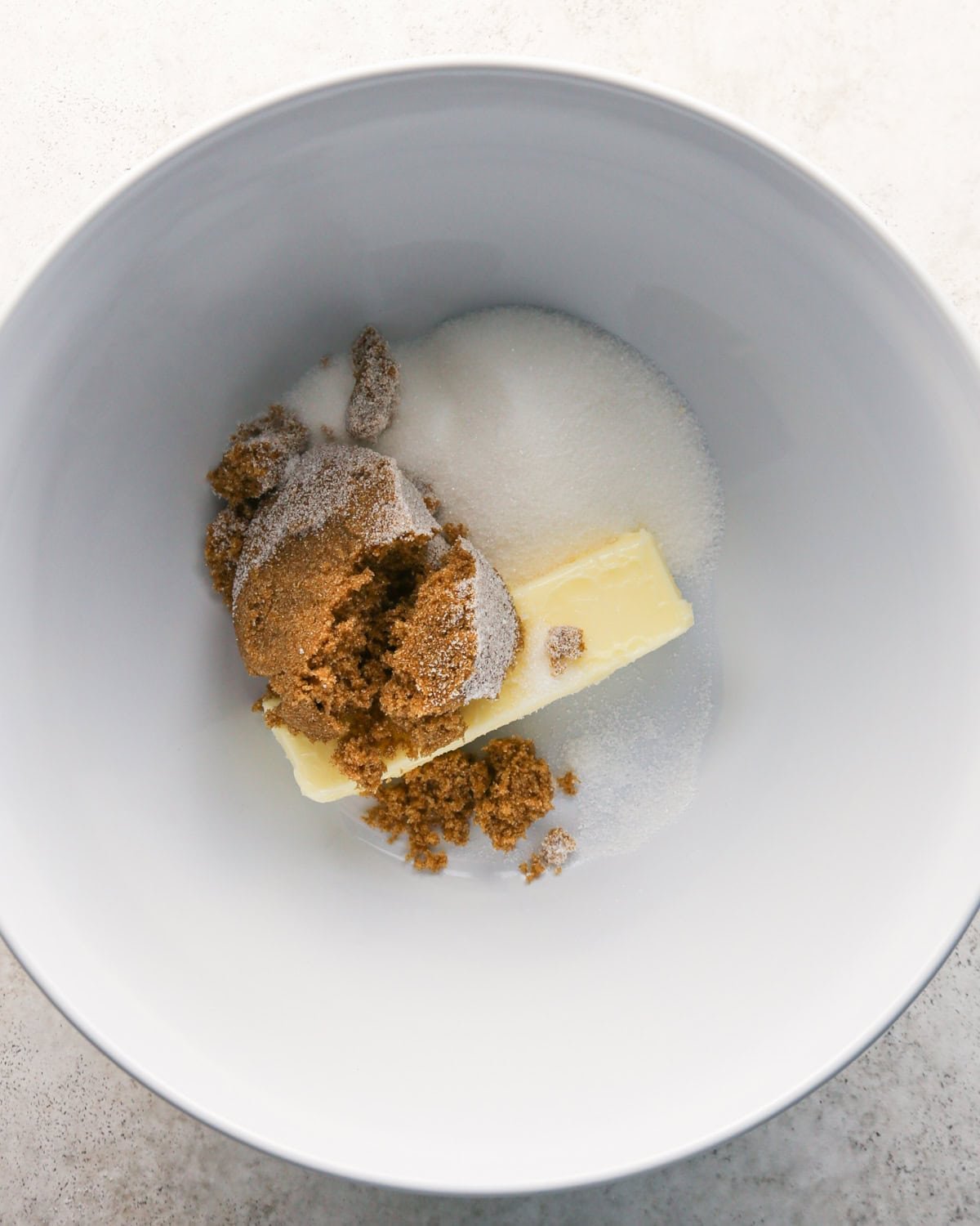 butter, brown sugar and white sugar in a white bowl on a gray surface before mixing making pumpkin snickerdoodles