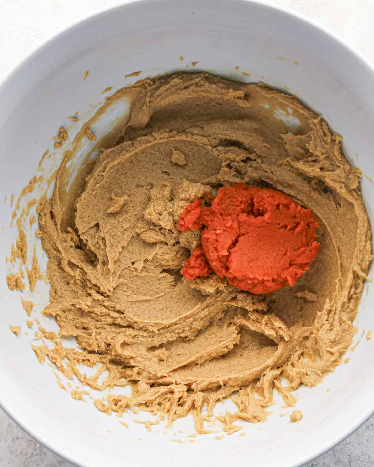 pumpkin puree added to the beaten butter, sugar, egg and vanilla mixture in a white bowl making pumpkin snickerdoodles