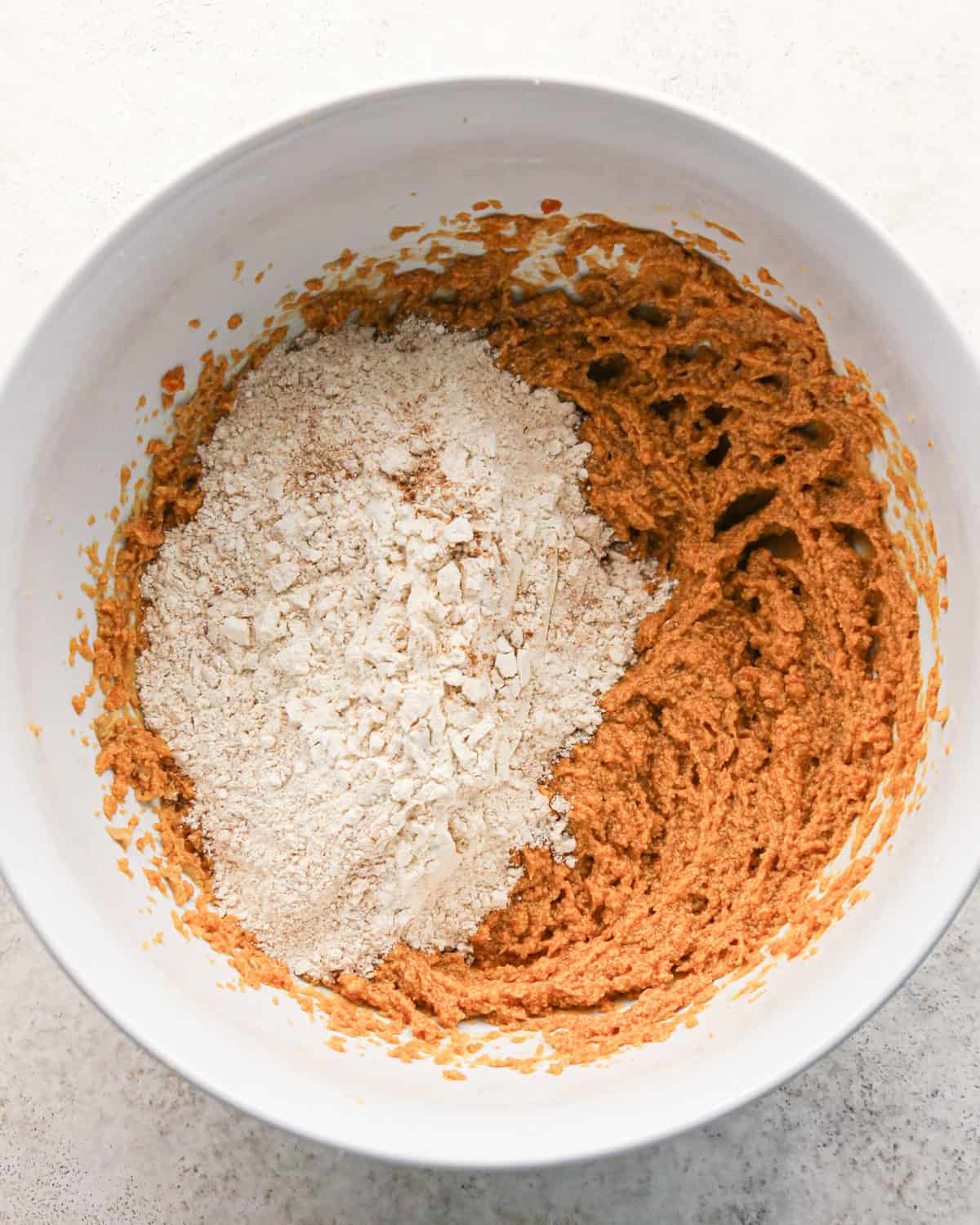 dry ingredients added to the wet ingredients before mixing in a white bowl on a gray surface making pumpkin snickerdoodles.
