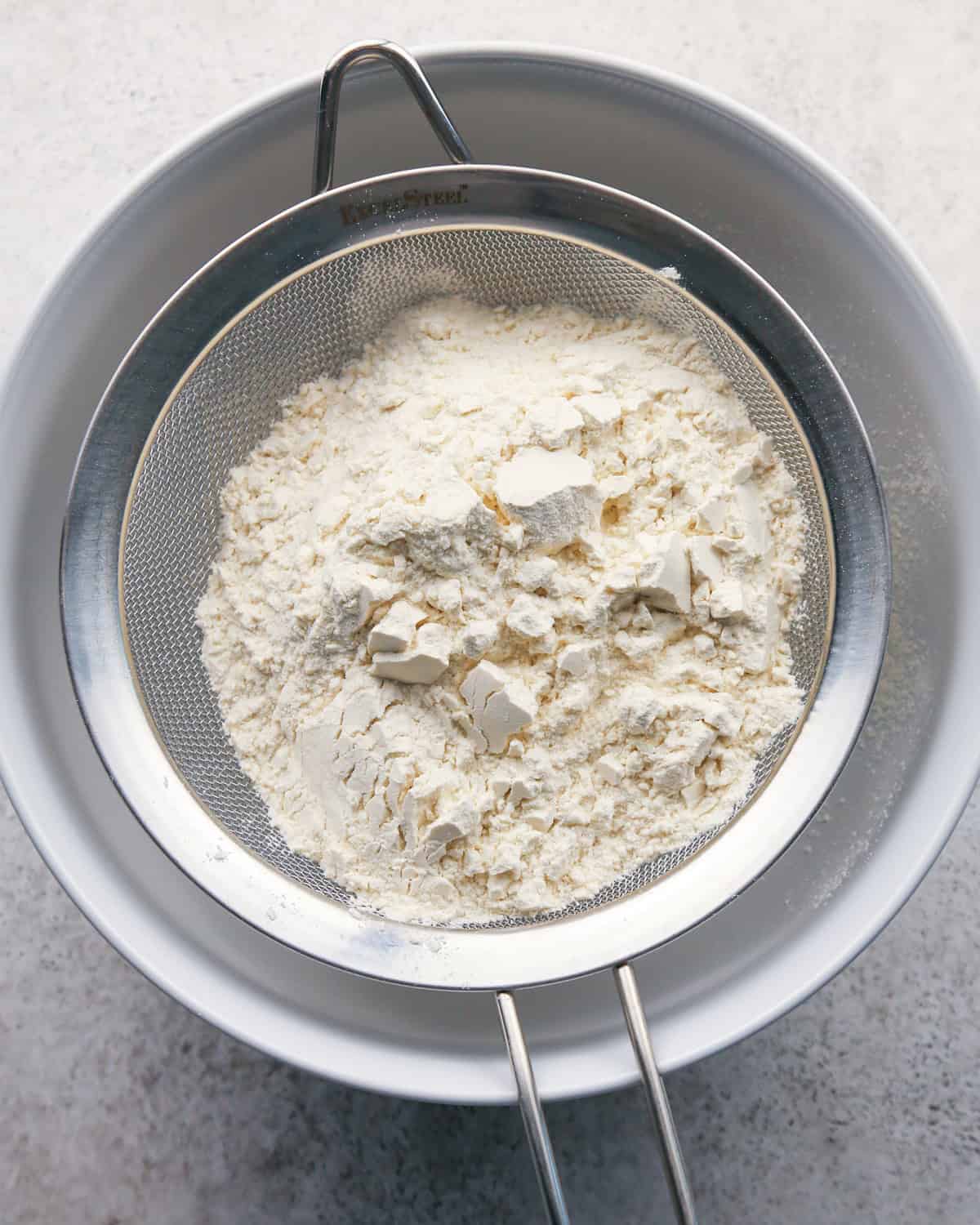 flour in a fine mesh metal strainer on a white bowl to make pumpkin snickerdoodles
