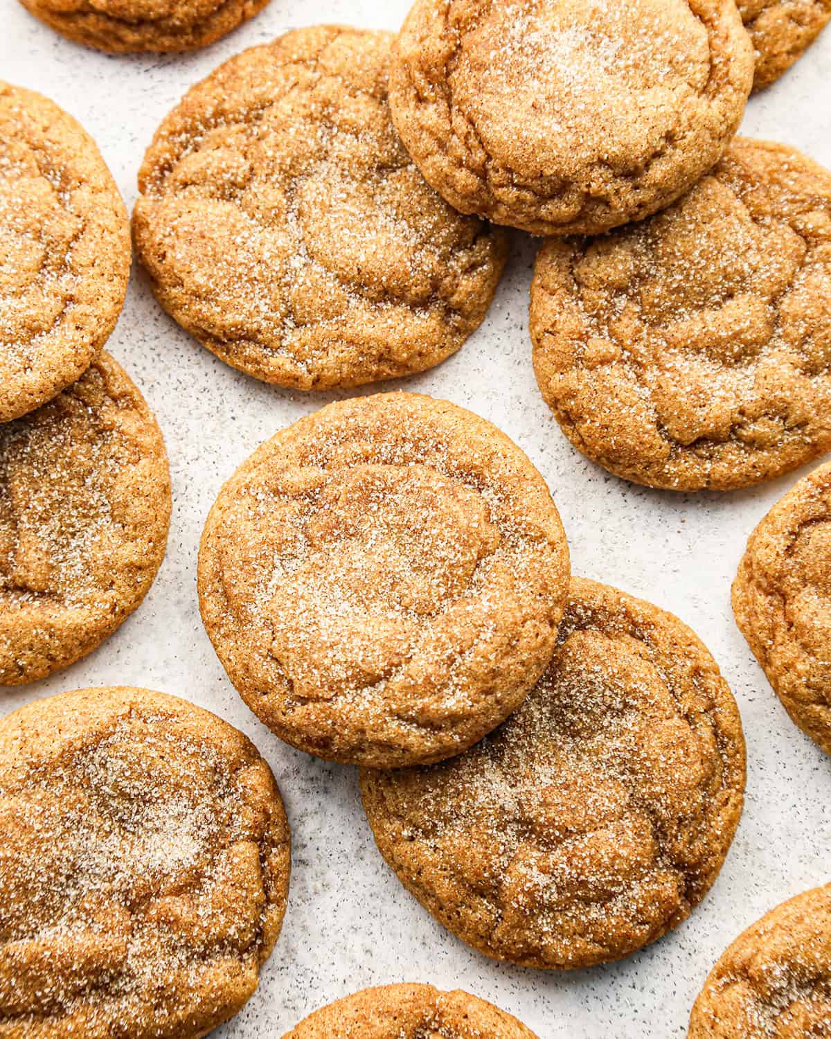 an overhead view of 10 pumpkin snickerdoodles arranged on a light surface. The cookies are golden brown, soft, and generously coated in cinnamon sugar, showcasing their crinkly texture