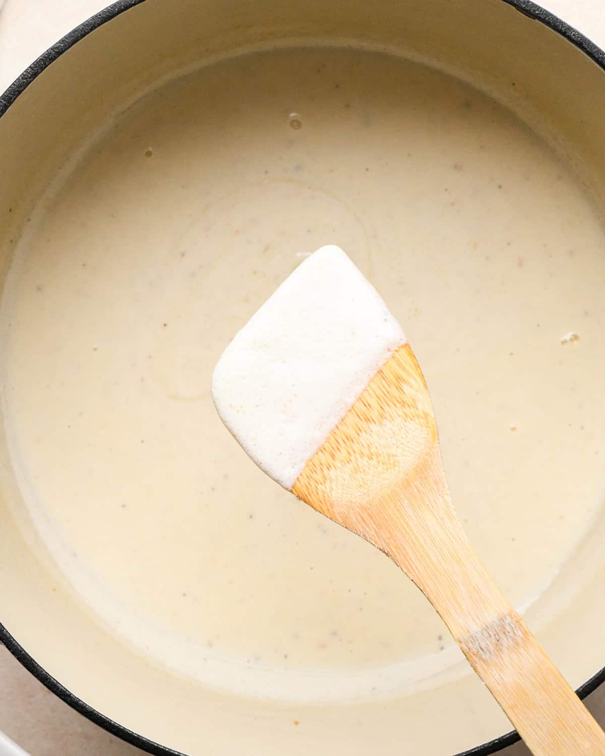 a wooden spoon coated in sauce being held over a pot of sauce making bacon mac and cheese