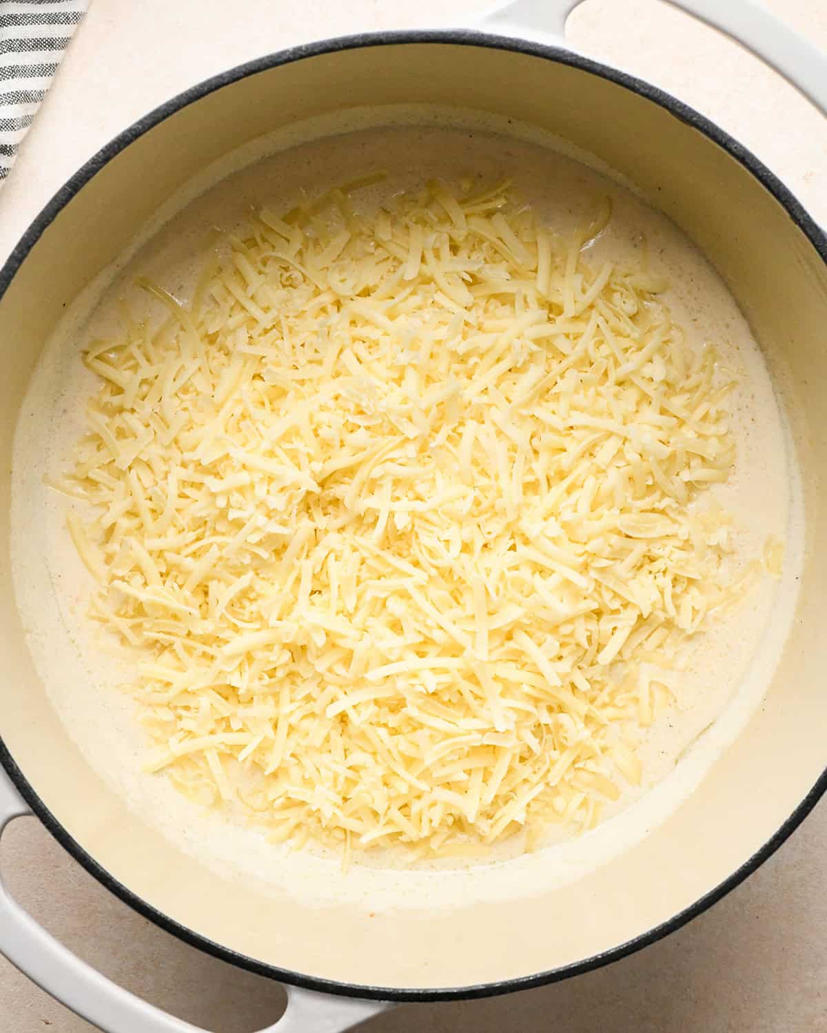 shredded white cheddar cheese added to the sauce in a white pot before mixing making bacon macaroni and cheese