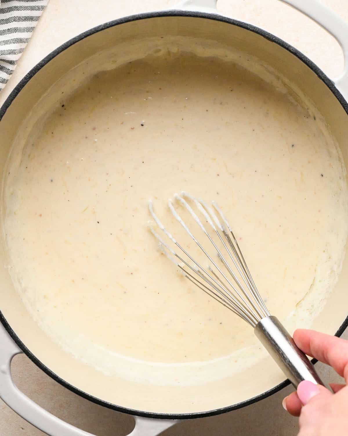 bacon macaroni and cheese sauce in a white pot being whisked by a hand with pink nails