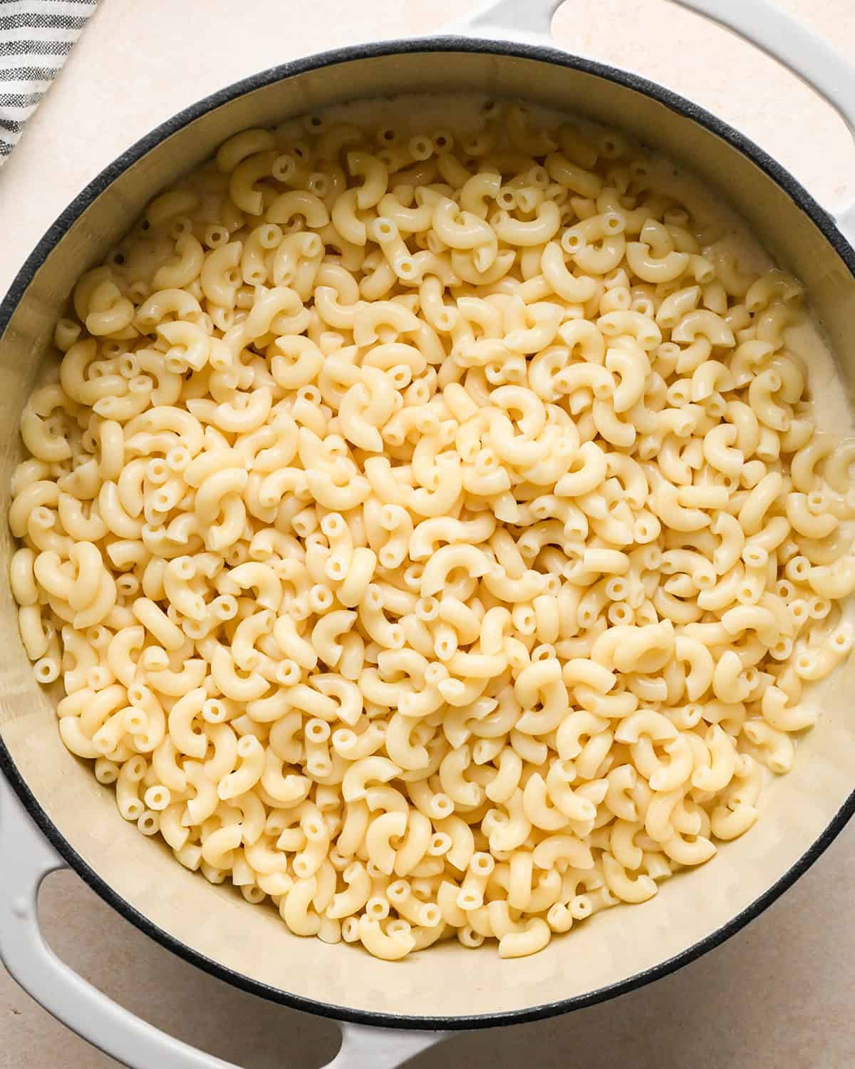 cooked macaroni noodles added to the cheese sauce in a white pot before mixing making bacon macaroni and cheese