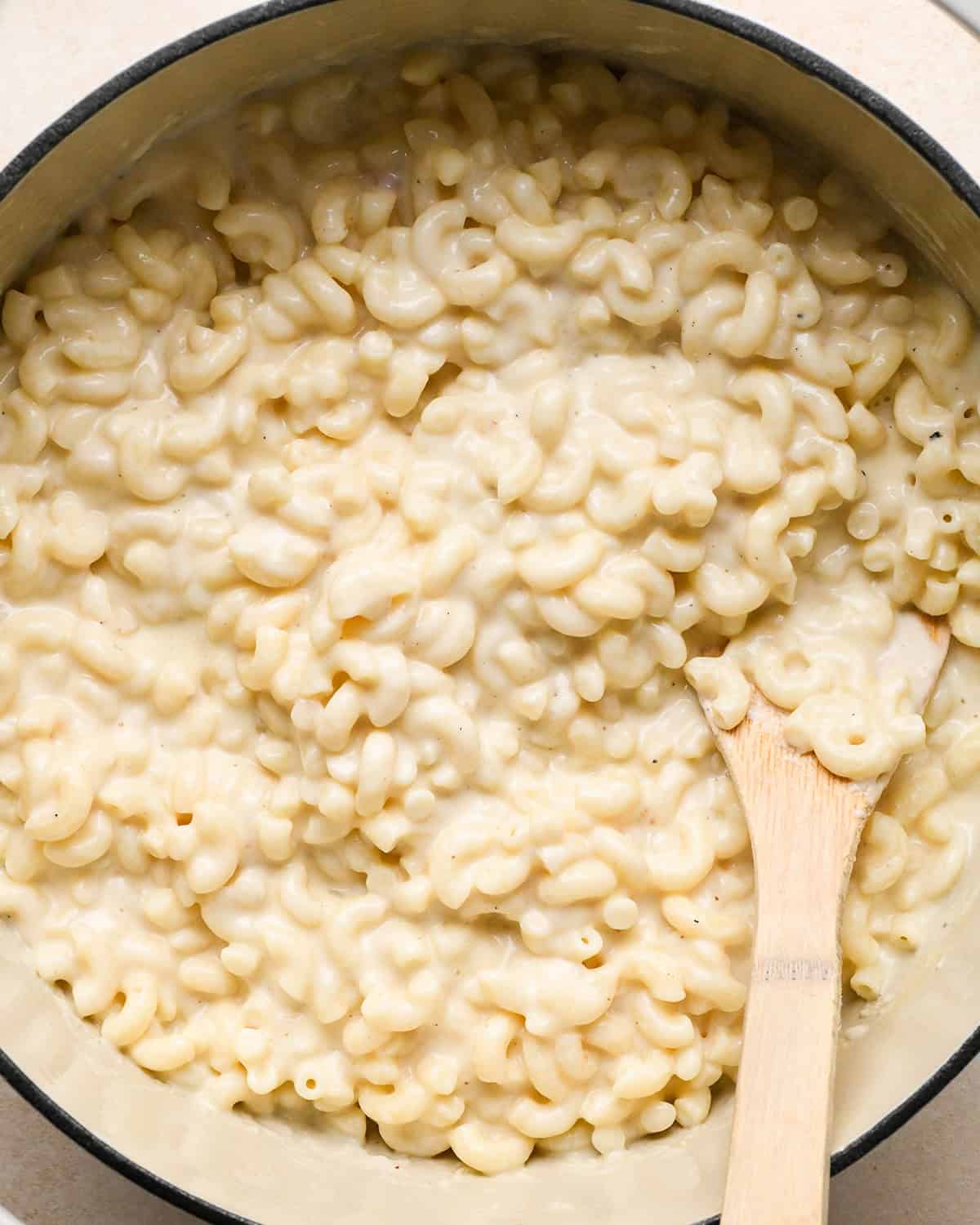 cheese sauce coating cooked macaroni noodles in a white pot making bacon macaroni and cheese