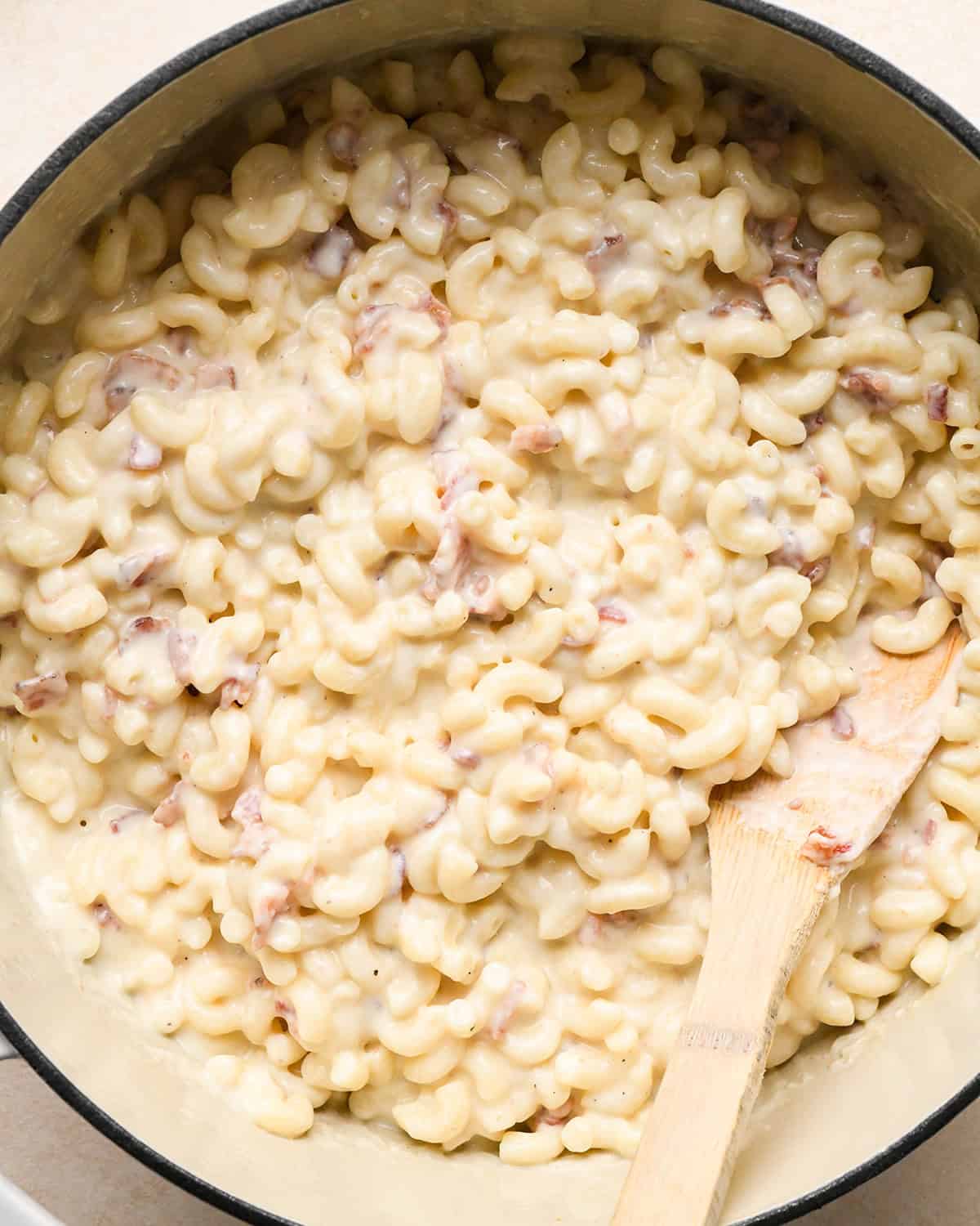 bacon macaroni and cheese in a white pot with a wooden spatula