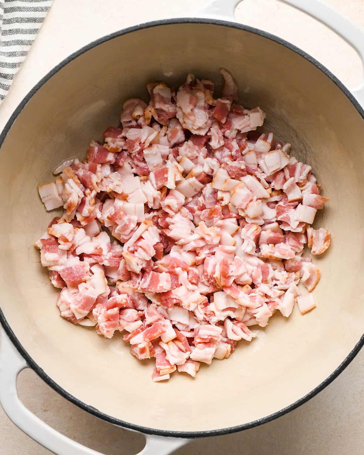 diced raw bacon in a white pot with a black rim to make bacon mac and cheese