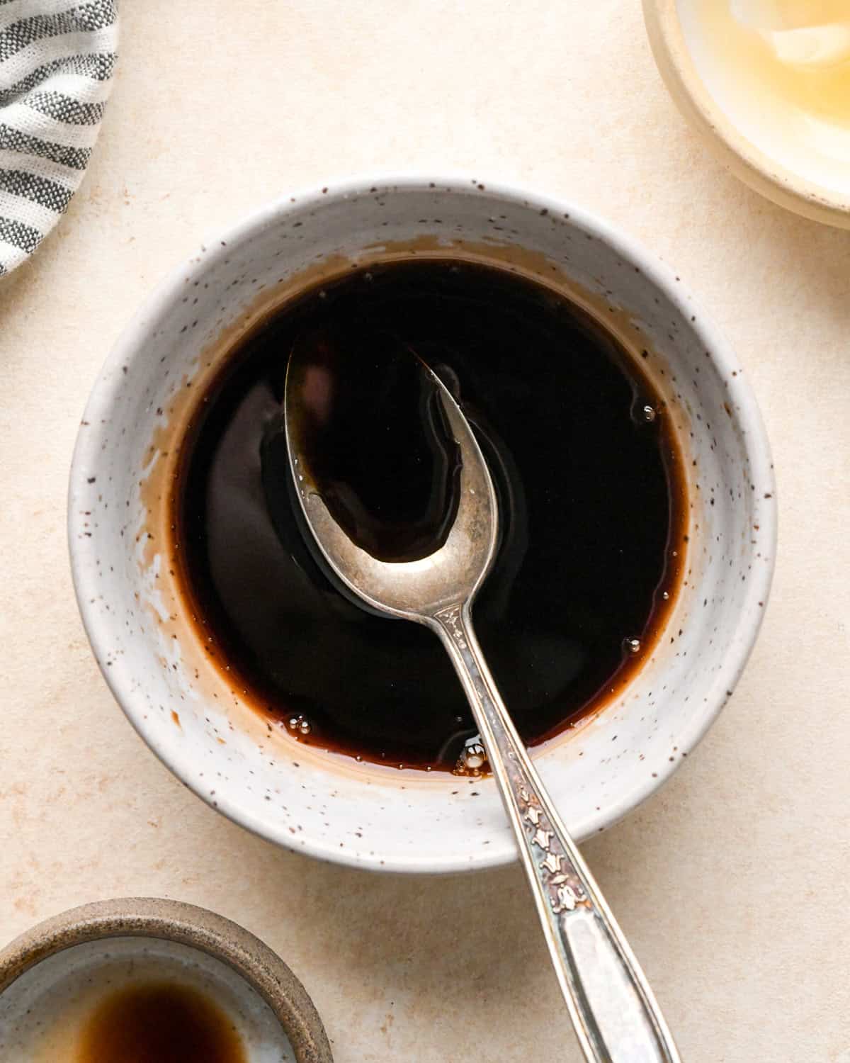 balsamic vinegar and honey in a white speckled ceramic bowl with a sliver spoon after mixing to use on roasted beets to put in a beet salad
