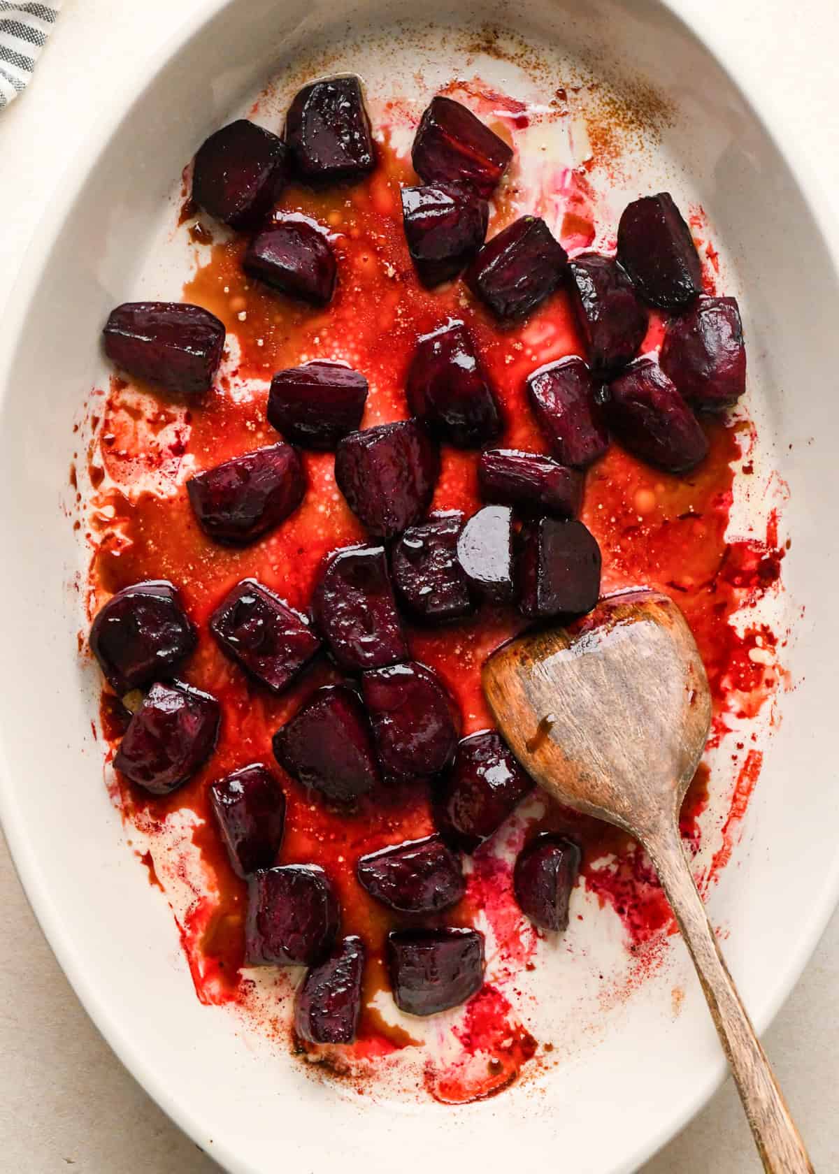 roasted beets in a white oval ceramic baking dish with a wooden spatula