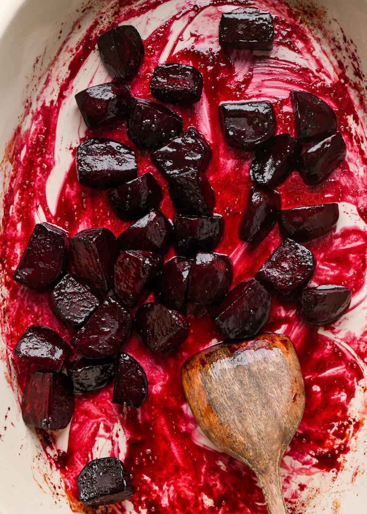 close up of balsamic roasted beets in a white oval ceramic baking dish with a wooden spatula