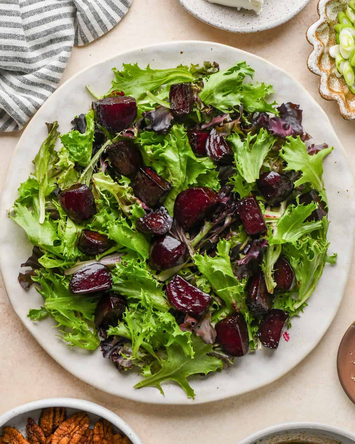 assembling beet salad - roasted beets added to spring mix on a white ceramic plate