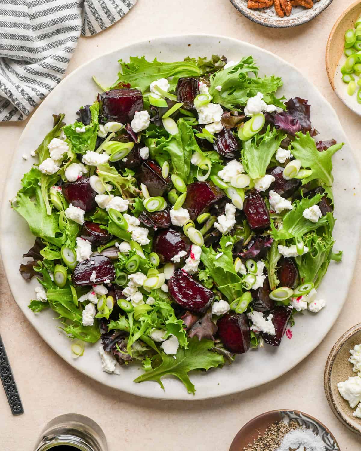 assembling beet salad - goat cheese added to spring mix and roasted beets on a white ceramic plate