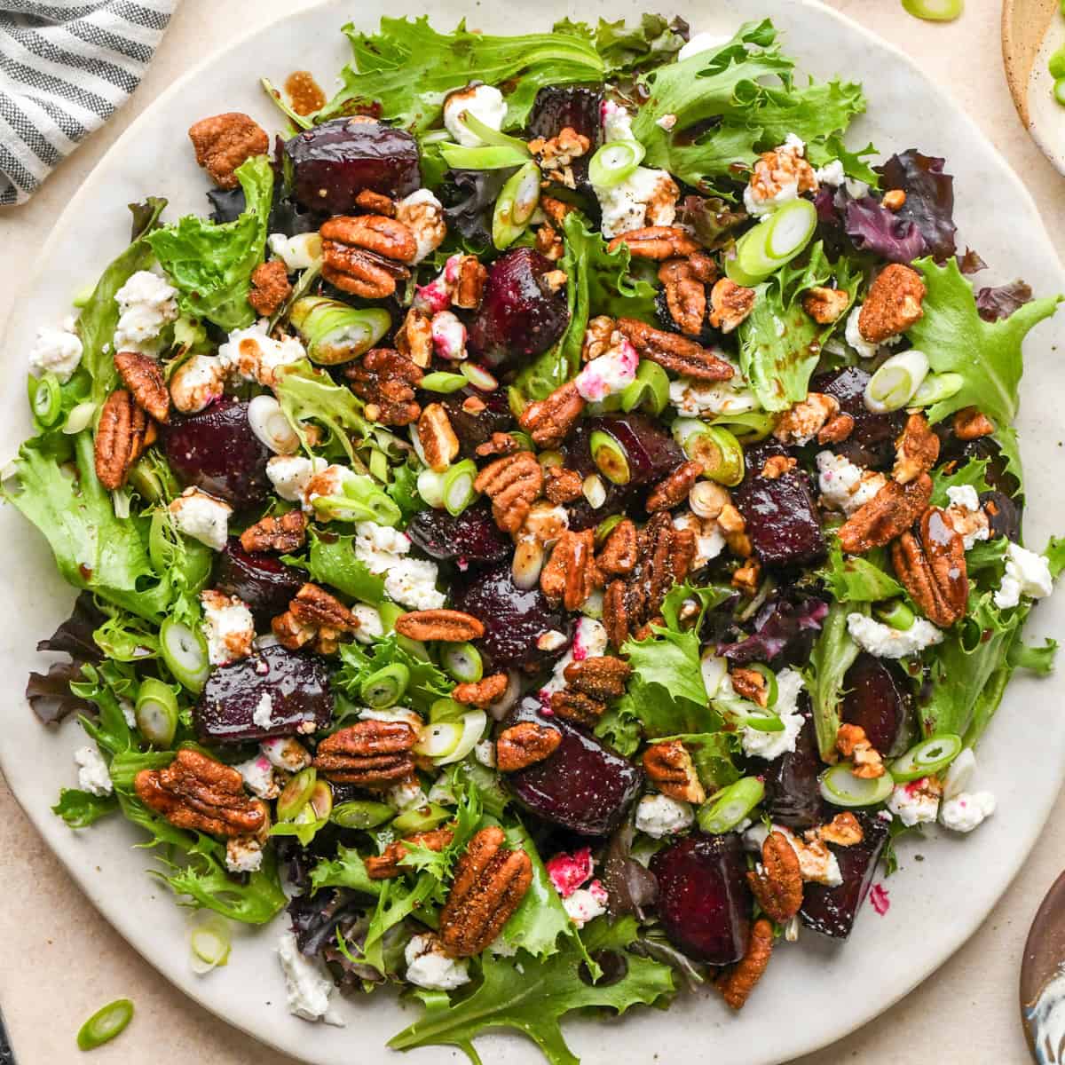 beet salad on a white plate, made with mixed greens, roasted beets, goat cheese, sliced green onions, and candied pecans.