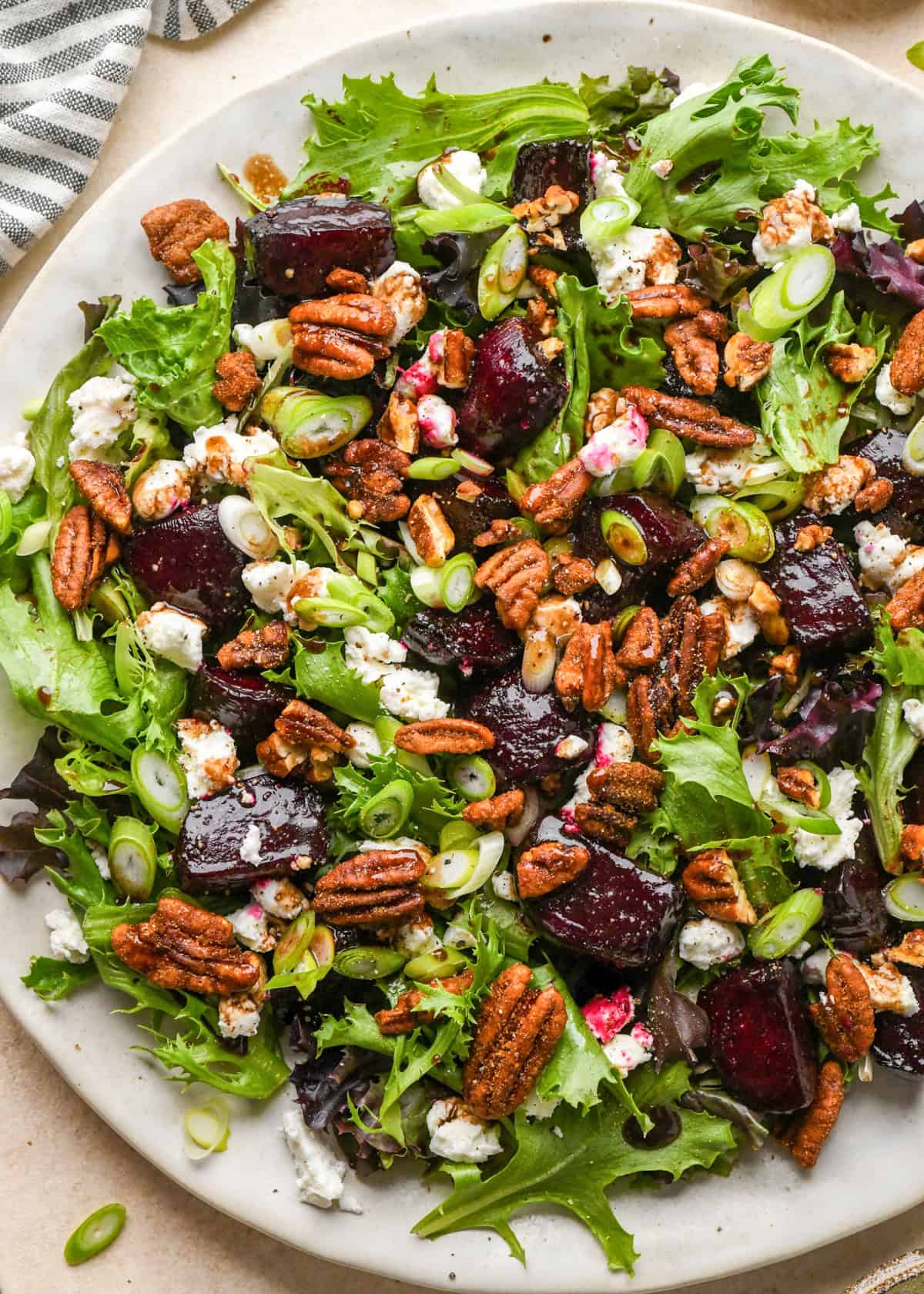 beet salad on a white plate, made with mixed greens, roasted beets, goat cheese, sliced green onions, and candied pecans.
