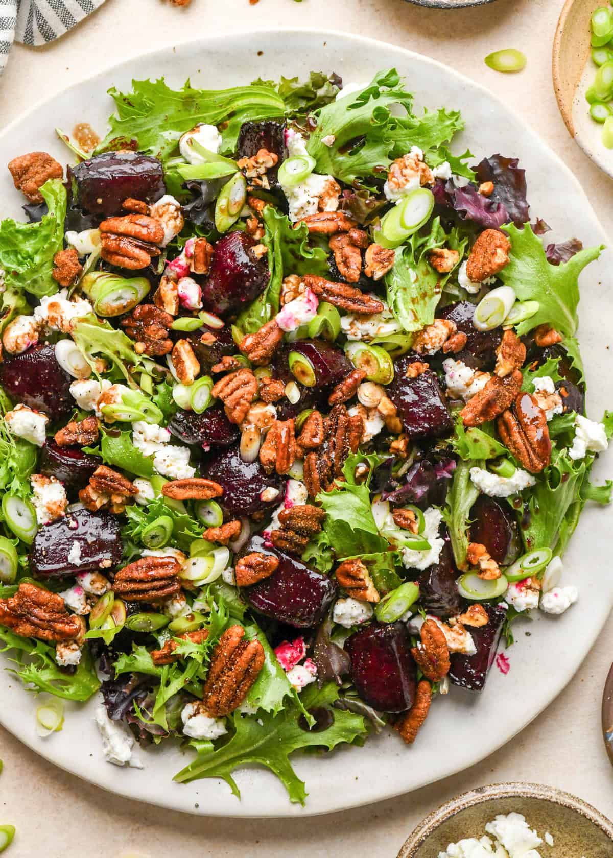 beet salad on a white plate, made with mixed greens, roasted beets, goat cheese, sliced green onions, and candied pecans.