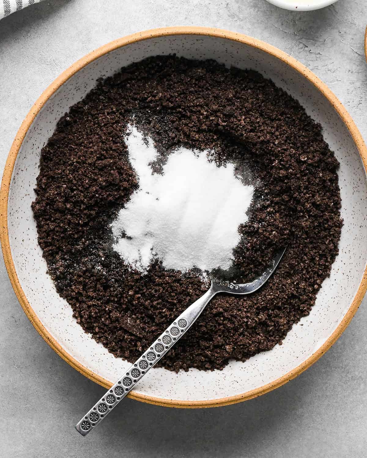 oreo crumbs, sugar and melted butter before mixing in a ceramic dish with a silver spoon to make the crust for chocolate peanut butter pie