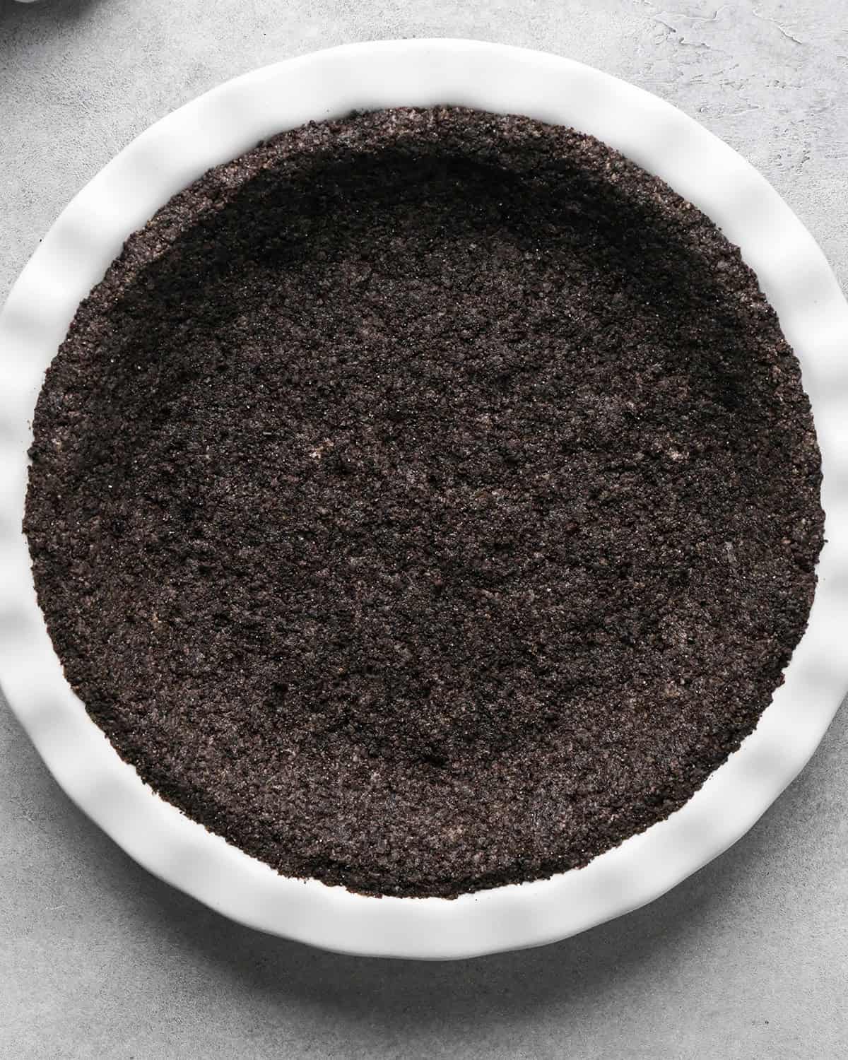 chocolate cookie crust in a white pie dish before baking making chocolate peanut butter pie