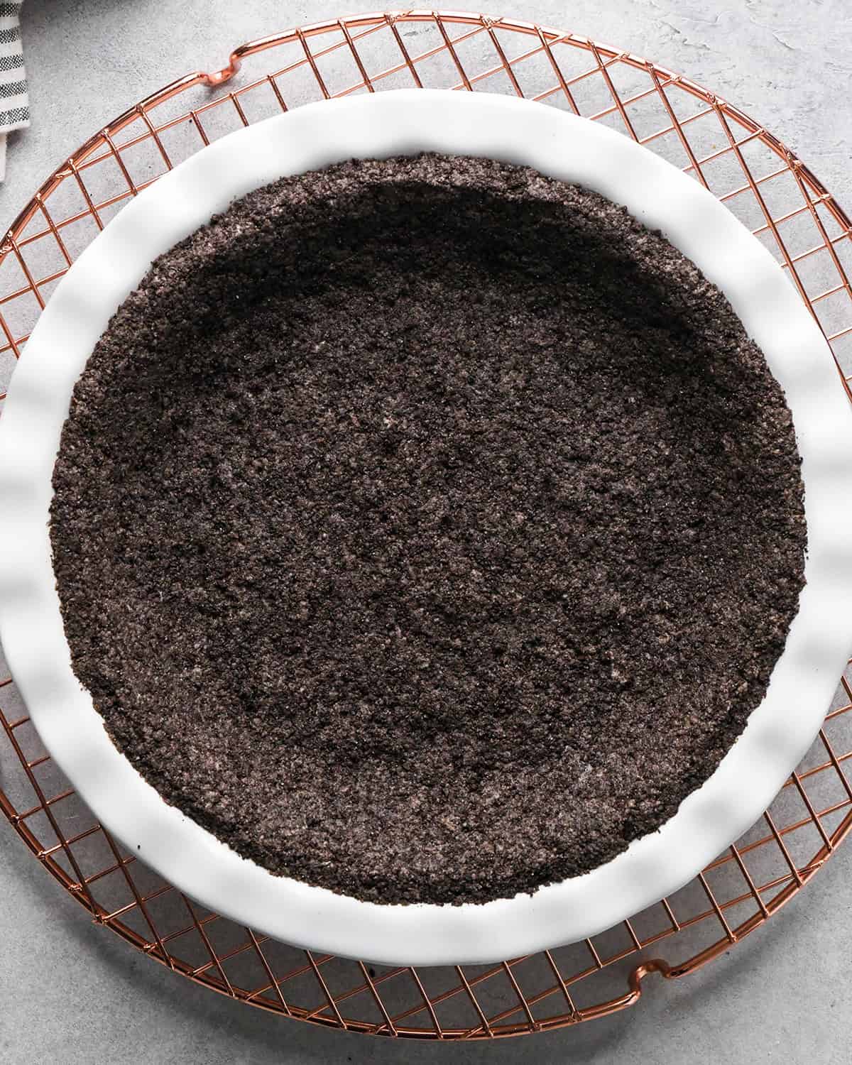 chocolate cookie crust in a white pie dish after baking on a wire cooling rack making chocolate peanut butter pie