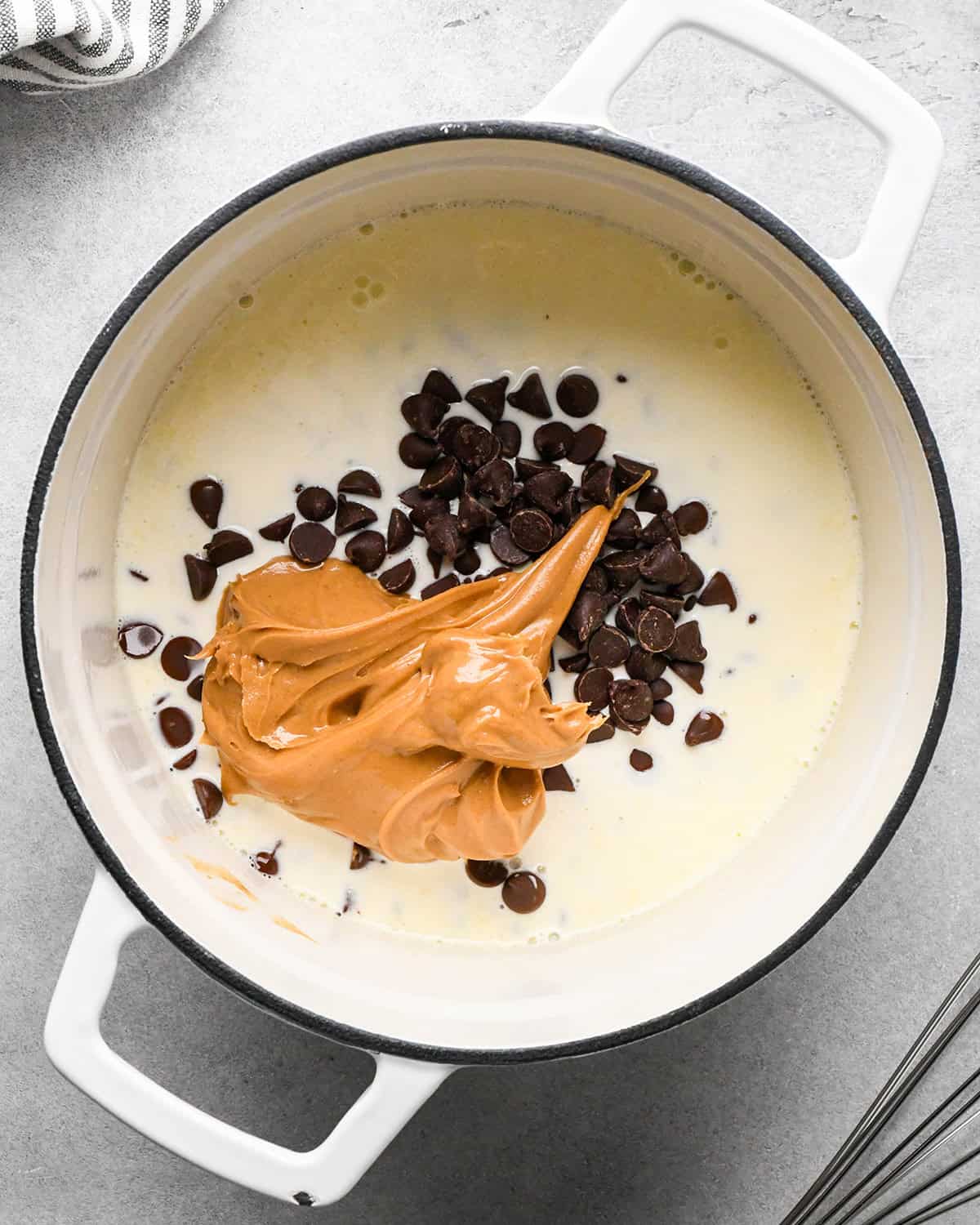 heavy cream, peanut butter and chocolate chips in a white pot with a black rim before whisking making the chocolate peanut butter ganache for chocolate peanut butter pie
