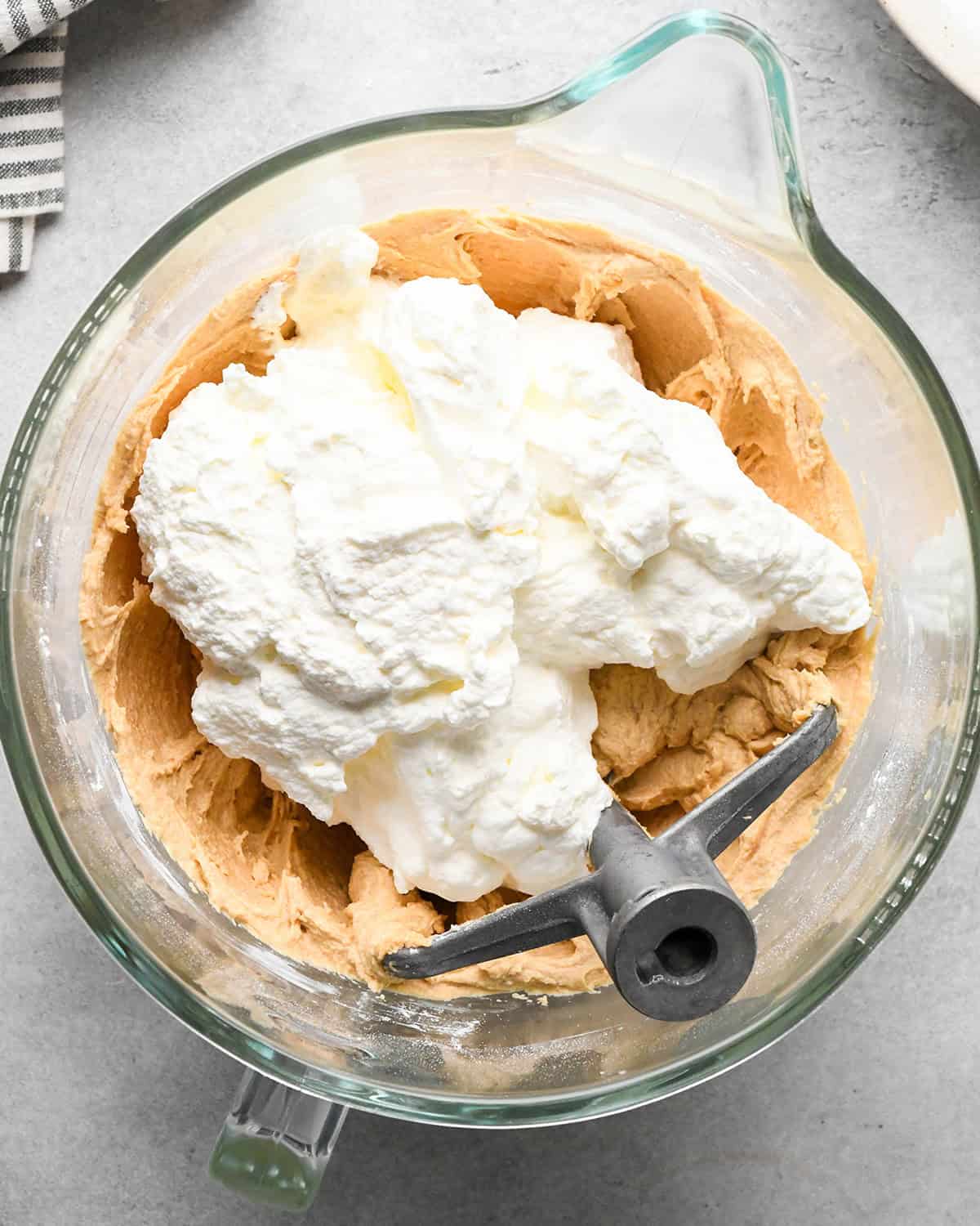 whipped cream added to the chocolate peanut butter pie filling before mixing in a glass mixing bowl with the paddle attachment on a gray surface