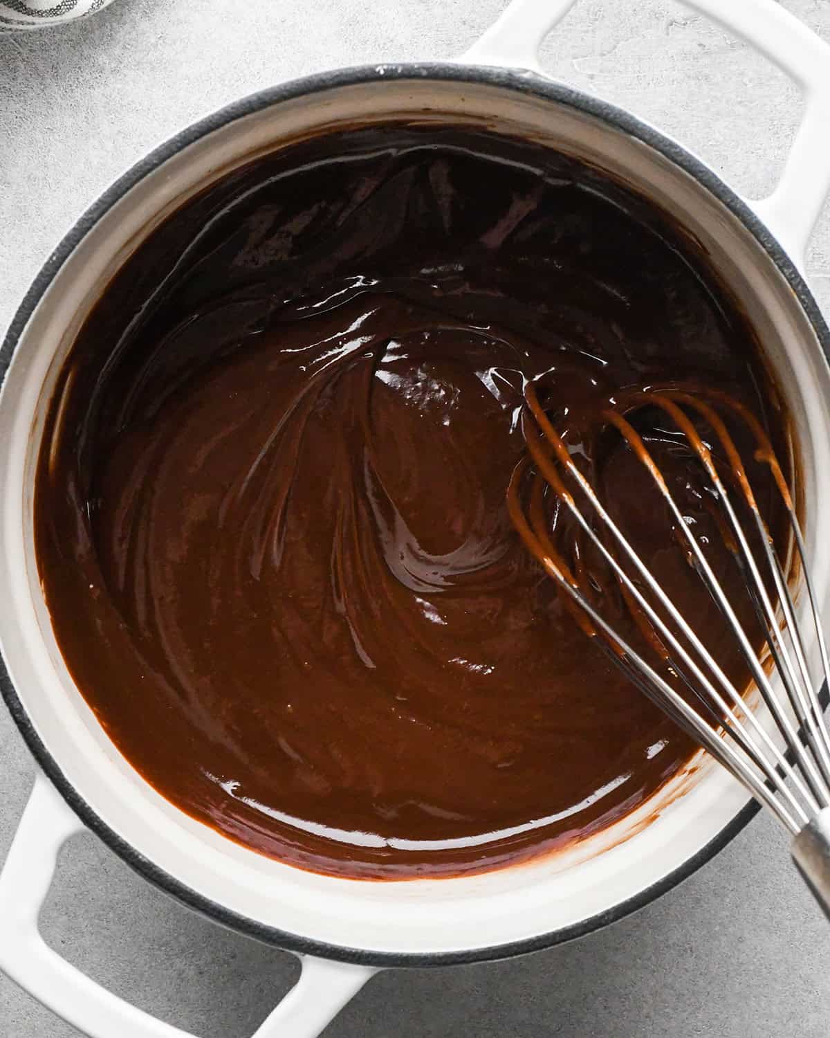 chocolate peanut butter ganache being whisked in a white pot with a black rim for chocolate peanut butter pie