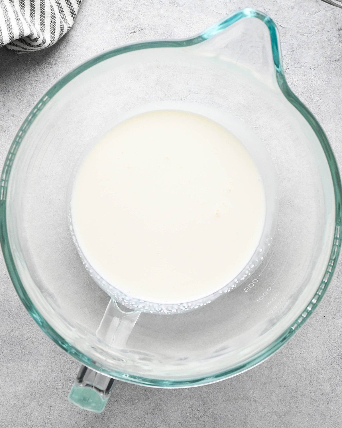 heavy whipping cream in a glass mixing bowl on a gray surface before whipping