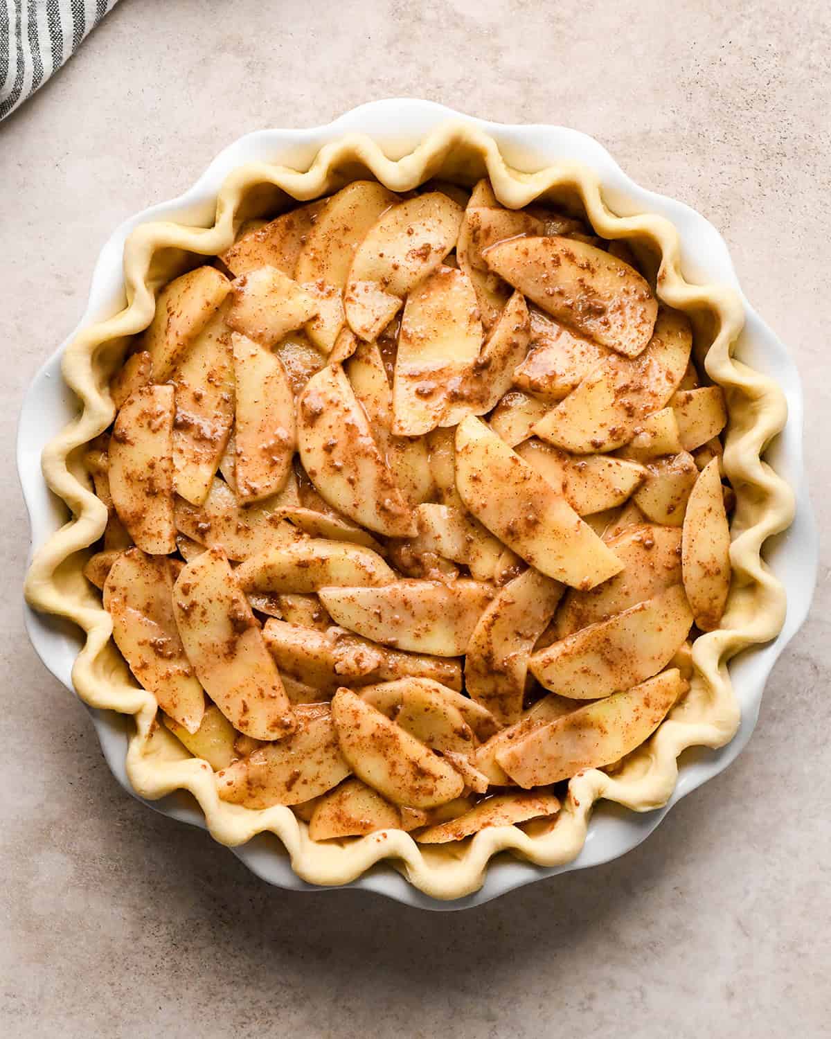 dutch apple pie filling added to a pie crust with a fluted edge in a white ceramic pie dish