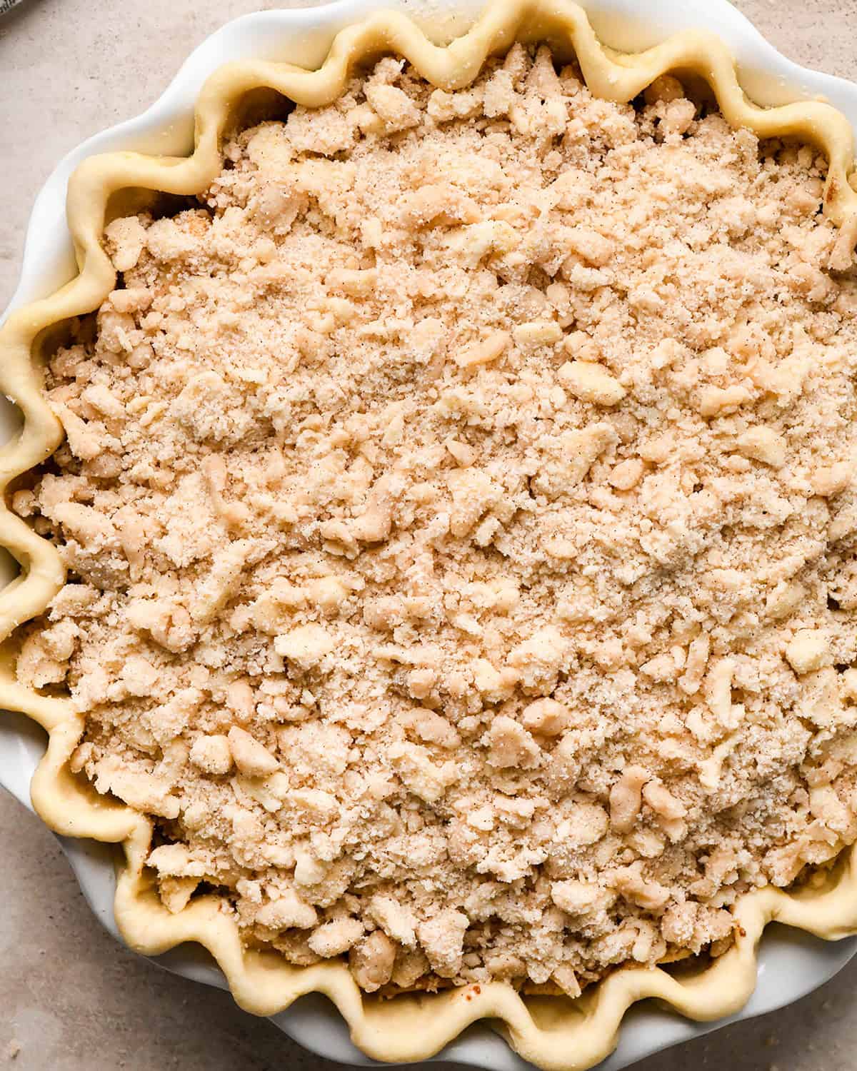 crumb topping over dutch apple pie filling in a pie crust with a fluted edge in a white ceramic pie dish