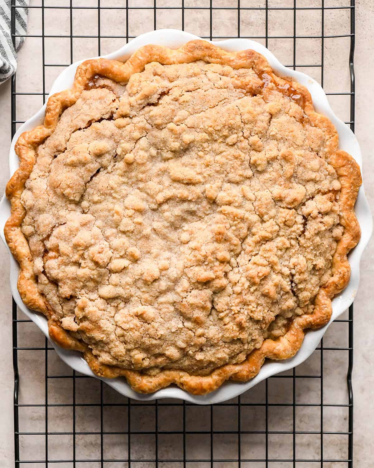 dutch apple pie in a white ceramic pie dish after baking on a black wire cooling rack