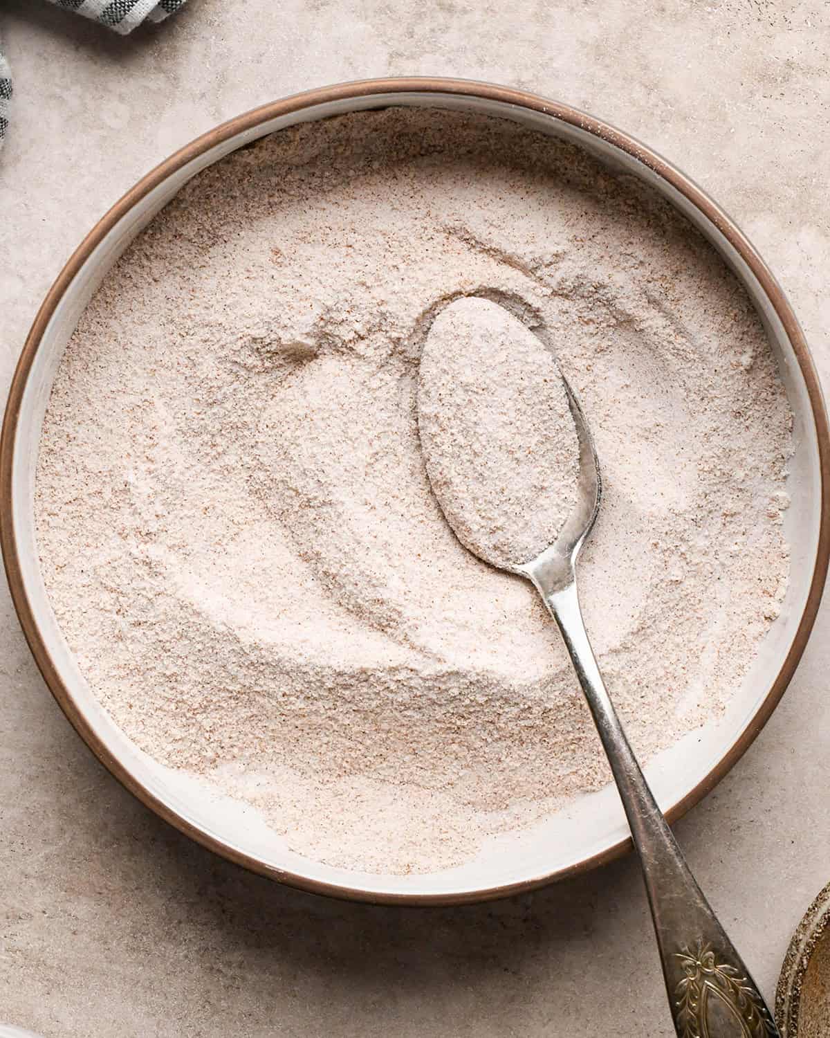 flour, sugar, cinnamon nutmeg and salt in a bowl on a tan surface after mixing with a silver spoon, making the dutch apple pie filling.
