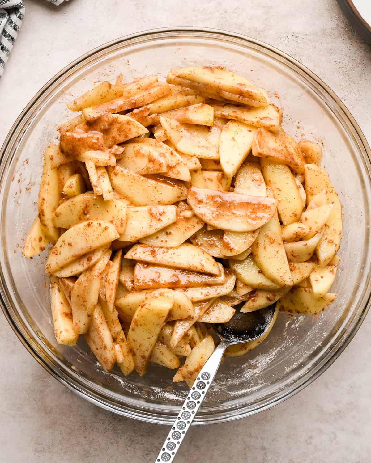 dutch apple pie filling in a glass bowl with a silver spoon in it on a tan surface