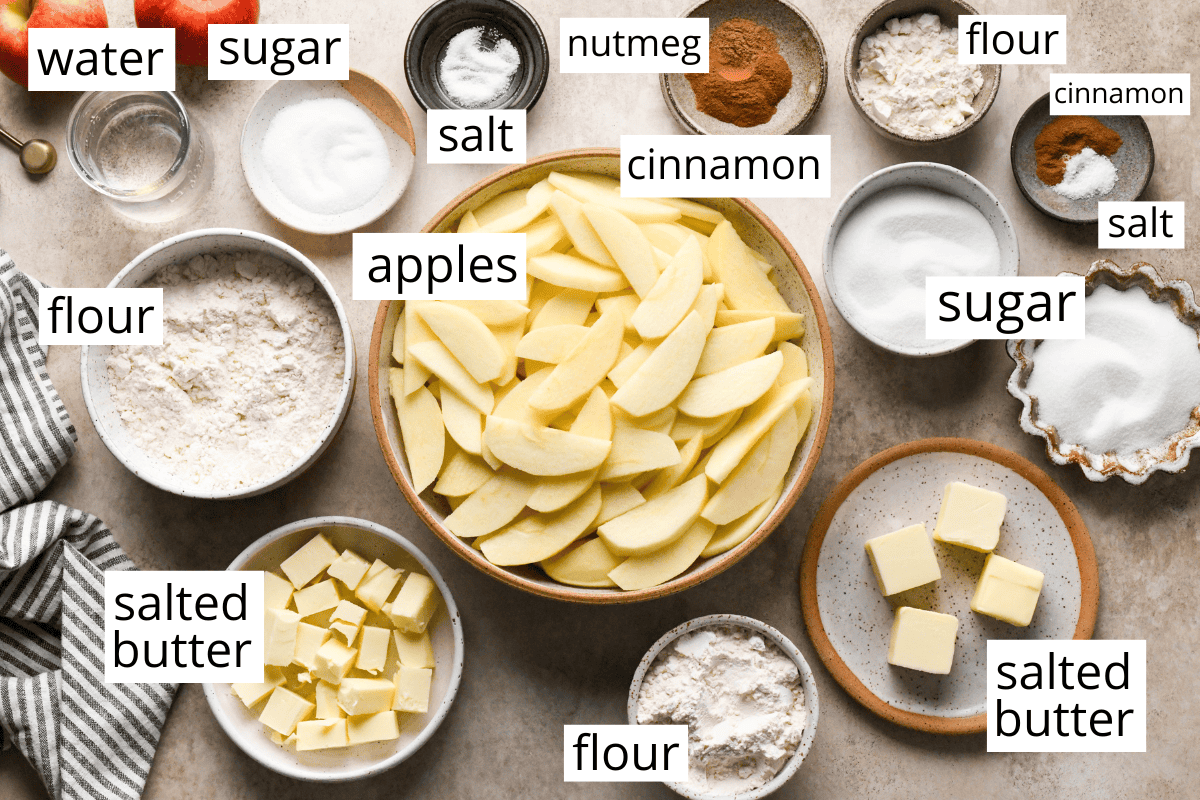 photo of the ingredients in this dutch apple pie recipe all in bowls and labeled like apples, flour, butter, cinnamon, nutmeg, water, sugar, and salt.