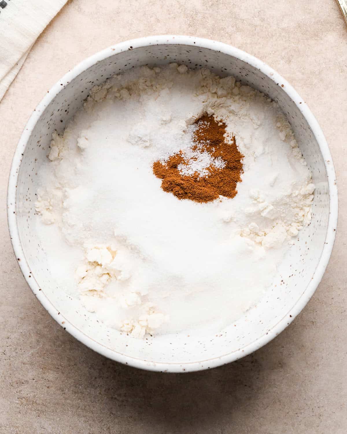 flour, sugar, cinnamon, salt and nutmeg in a speckled ceramic bowl before mixing on a tan surface making the dutch apple pie topping