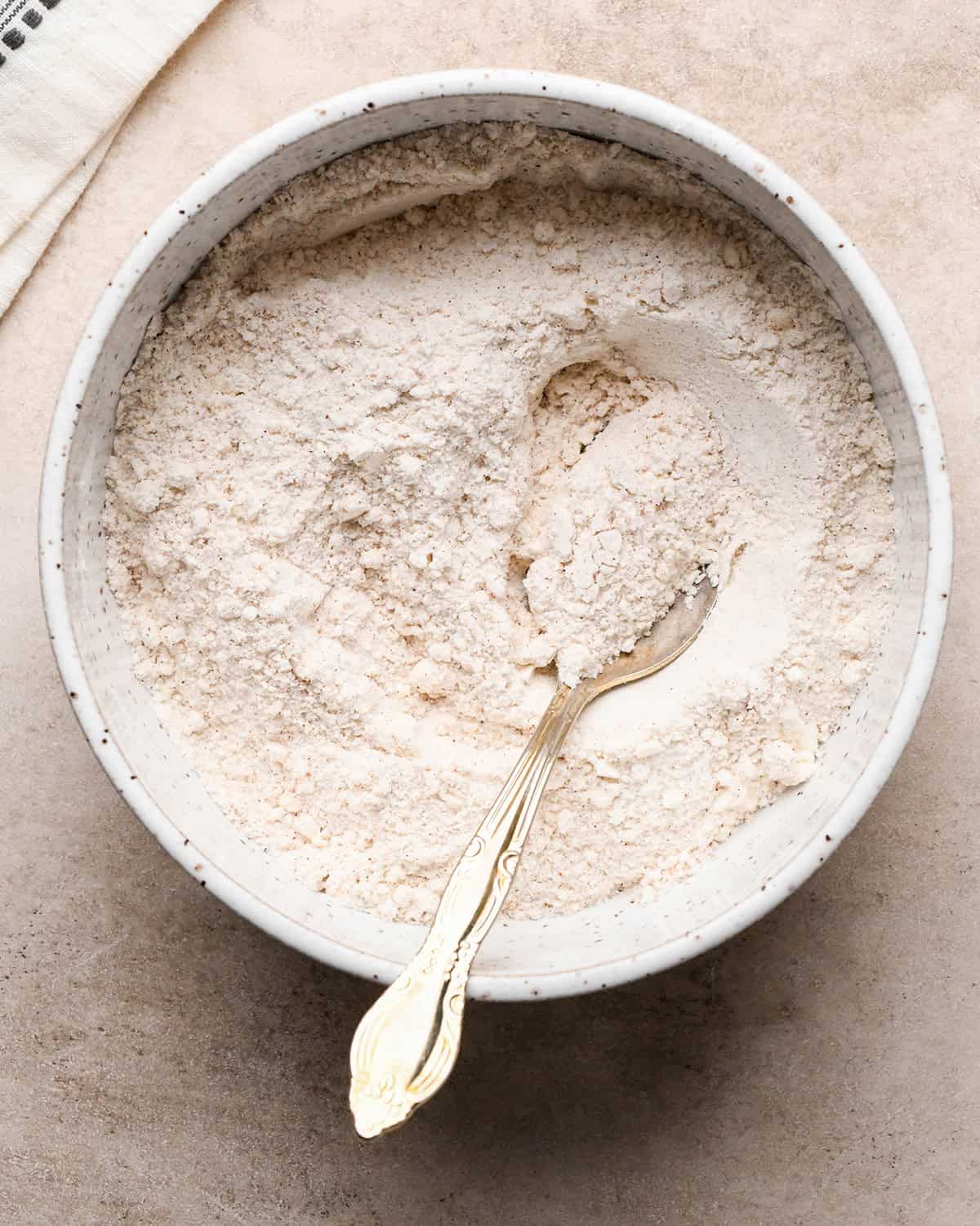 flour, sugar, cinnamon, salt and nutmeg in a speckled ceramic bowl after mixing with a silver spoon on a tan surface making the dutch apple pie topping