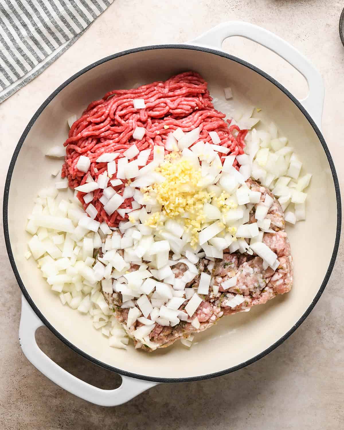 Making baked ziti - onion, garlic, Italian sausage, and ground beef in a white saucepan