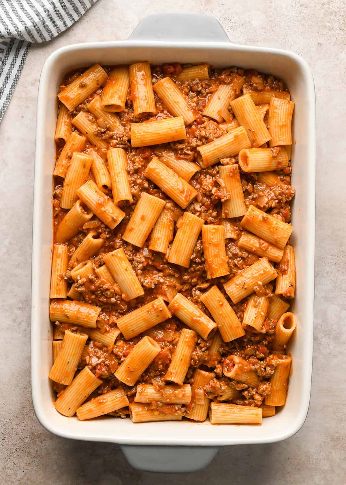 Making baked ziti - cooked ziti and sauce are poured into a white casserole dish and spread out evenly.