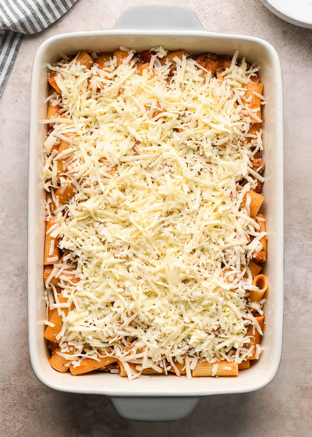 Making baked ziti - cooked ziti and sauce are poured into a white casserole dish and topped with mozzarella cheese.