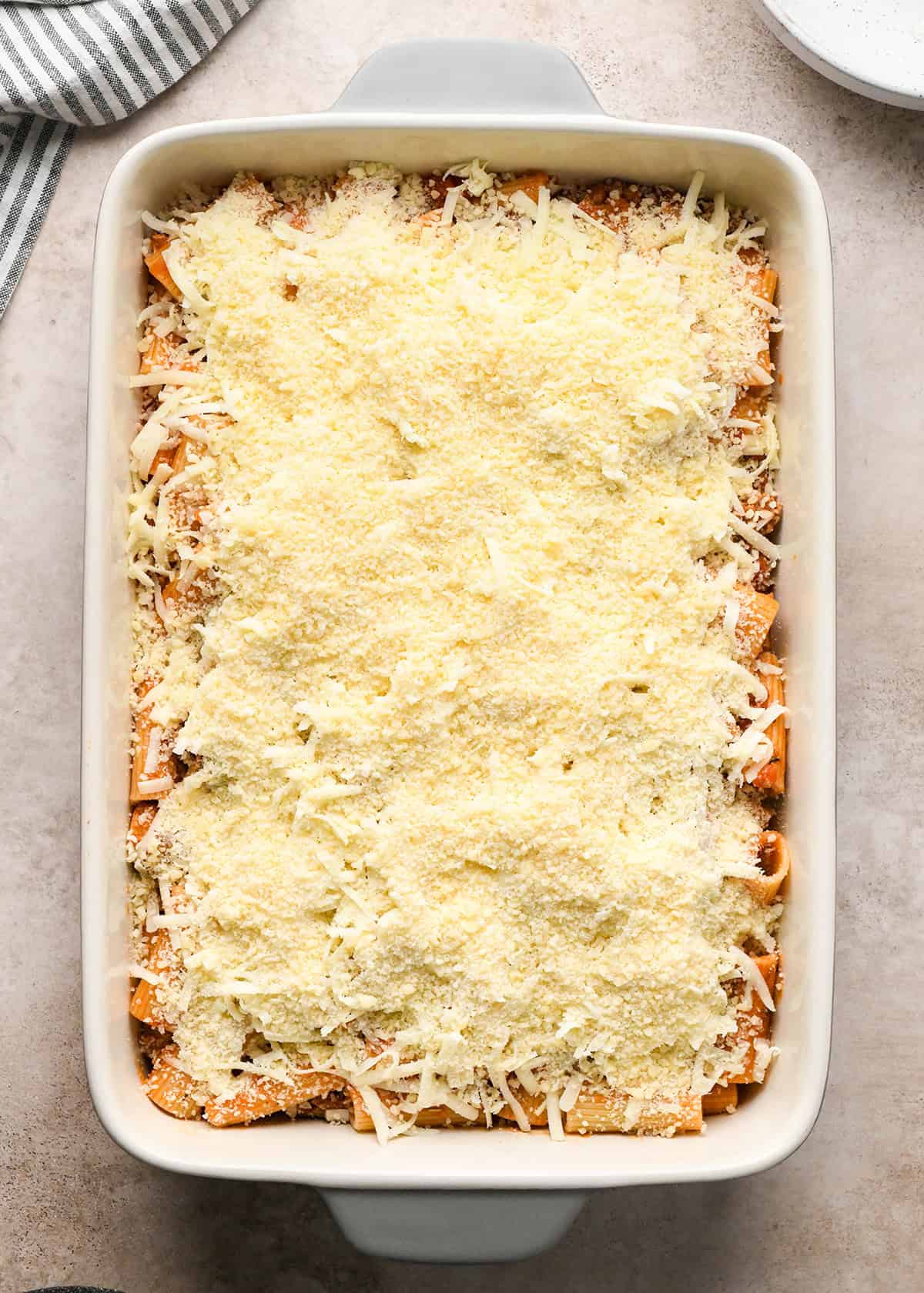 Making baked ziti - cooked ziti and sauce in a white casserole dish and topped with mozzarella cheese and then parmesan cheese.