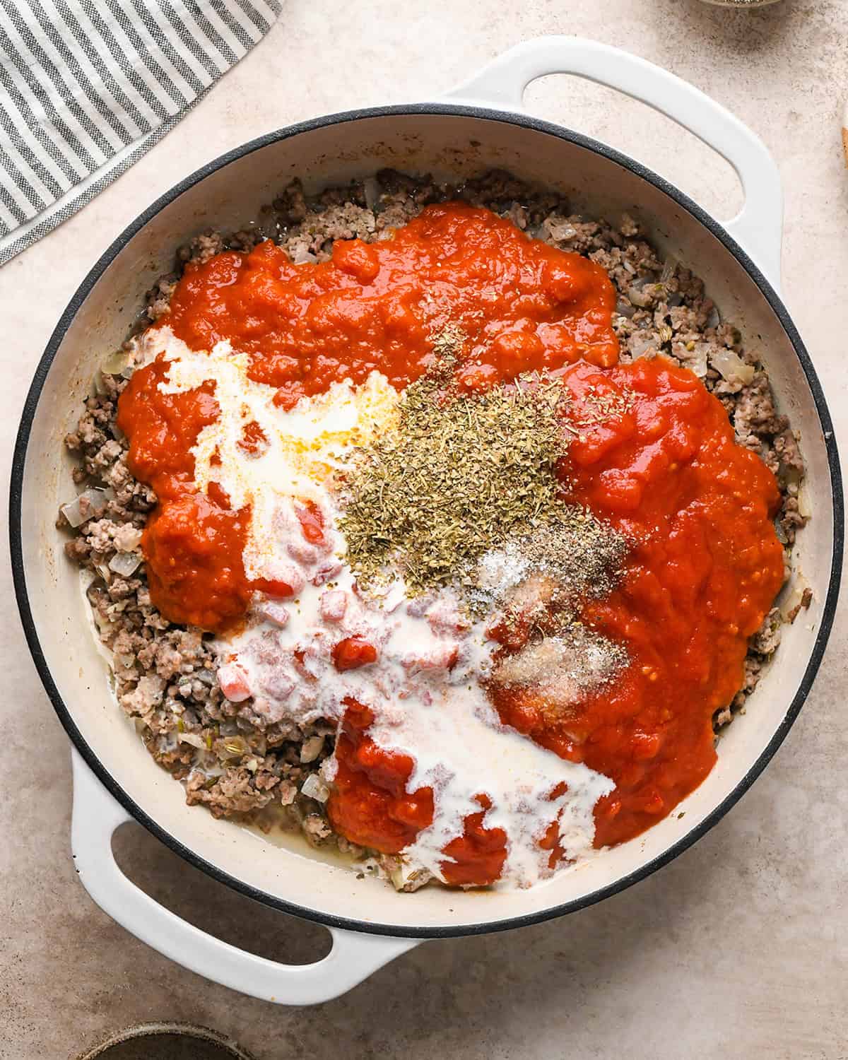 Making baked ziti - marinara sauce, crushed tomatoes, heavy cream, salt, pepper, and Italian seasoning are added to a saucepan